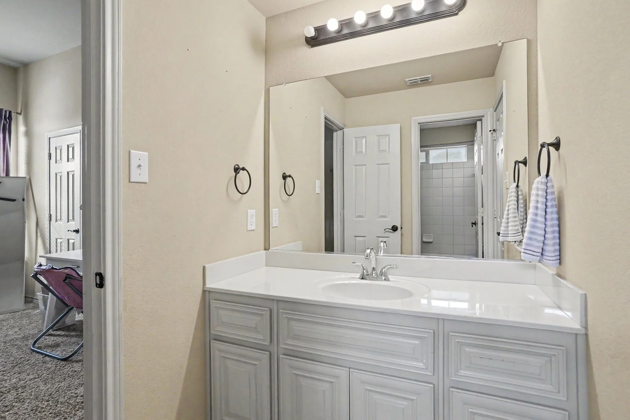 Bathroom vanity featuring a light-colored countertop, an undermount sink with a chrome faucet, and white paneled cabinetry