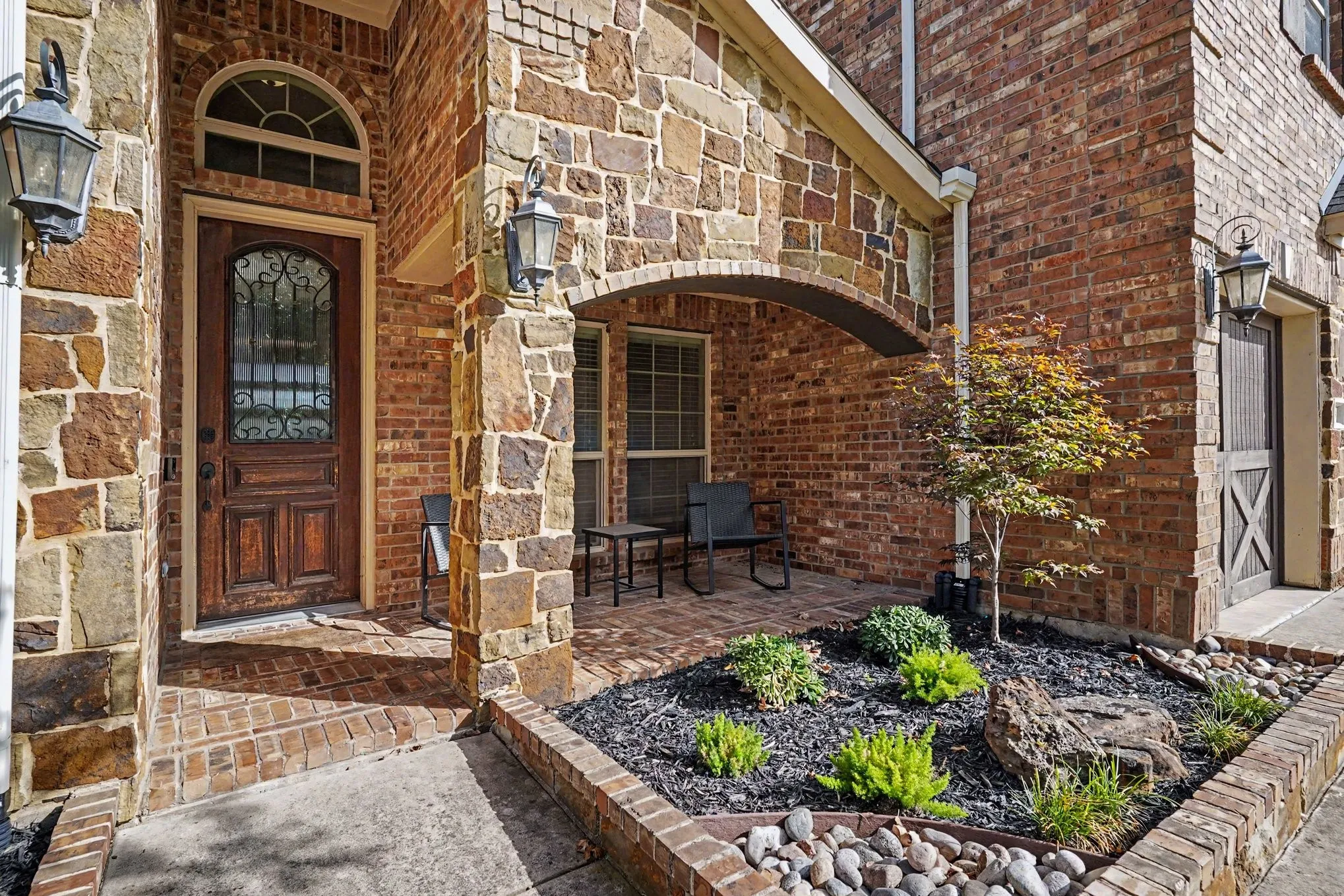 Stone and brick facade featuring an arched entry, a decorative wood door with ironwork, and a covered porch