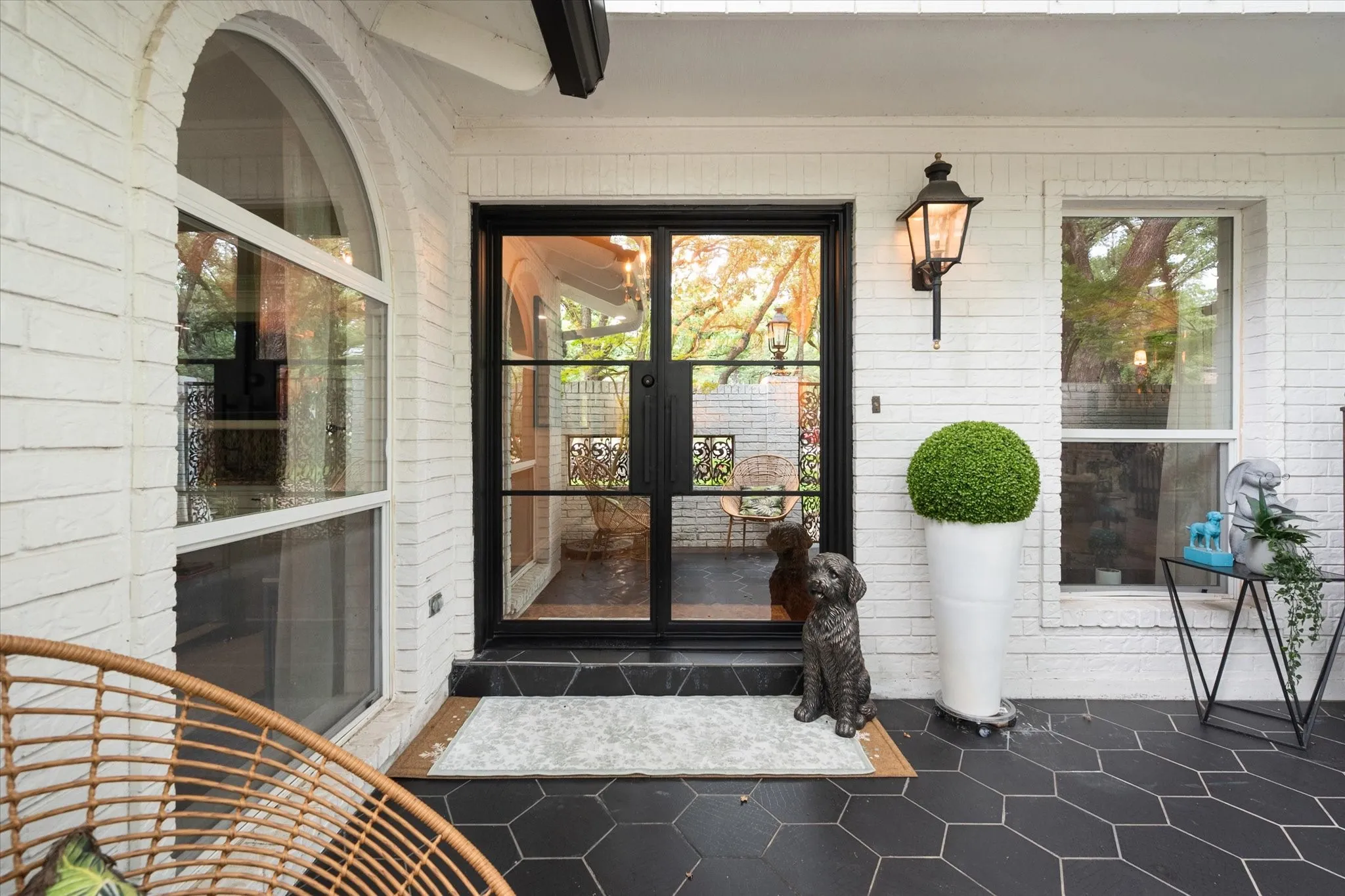 Entryway featuring a black-framed double door with glass panels, white brick exterior, black hexagonal floor tiles, and an arched window