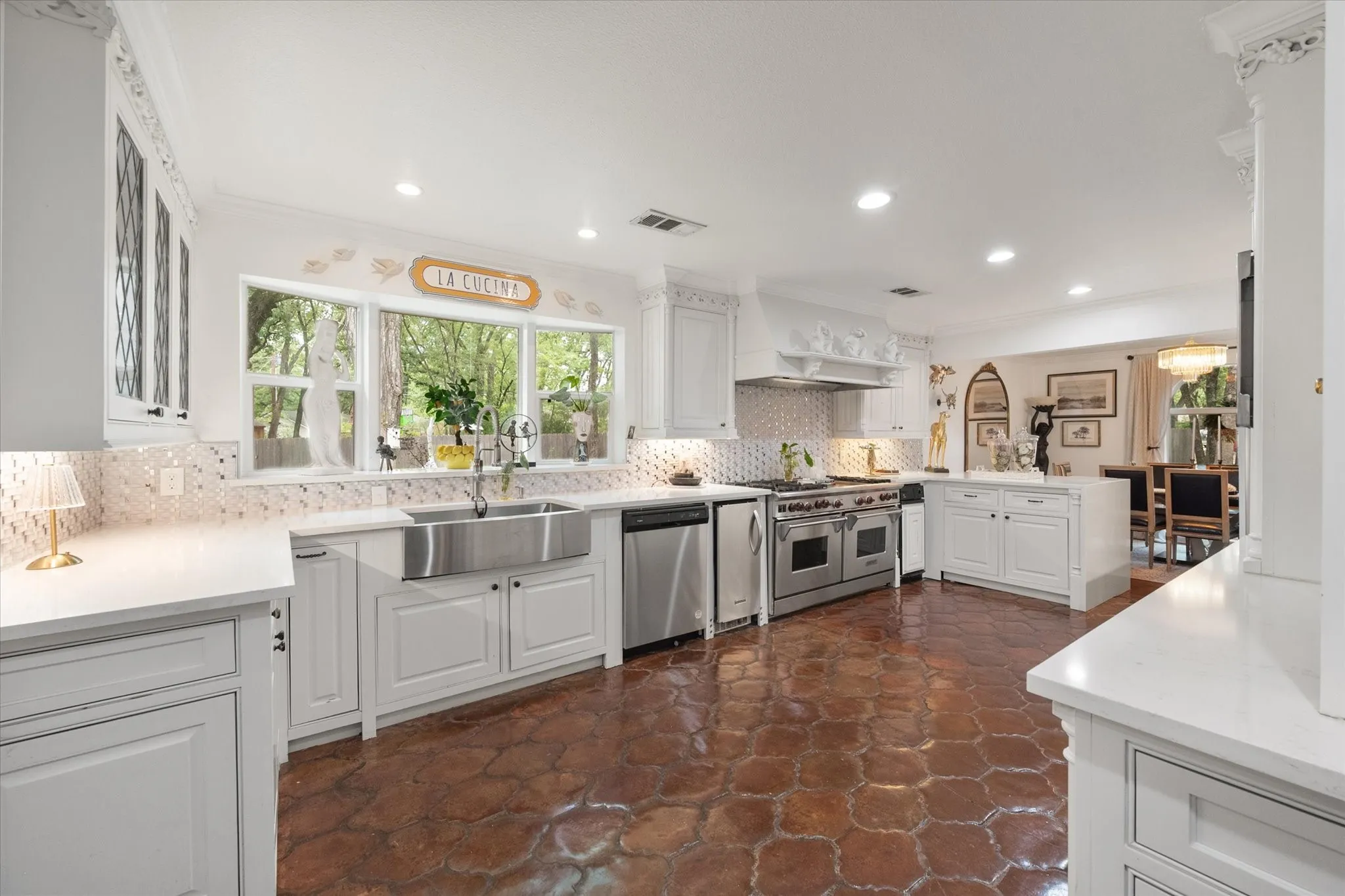 Spacious kitchen featuring white cabinetry, light countertops, stainless steel appliances, a double basin farmhouse sink, and terracotta-style flooring