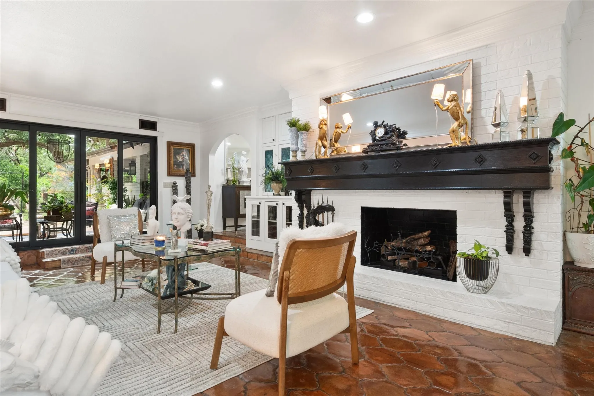 Living area featuring terracotta-style floor tiles, a white brick fireplace with a dark wood mantel, and large black-framed glass doors opening to outdoor space
