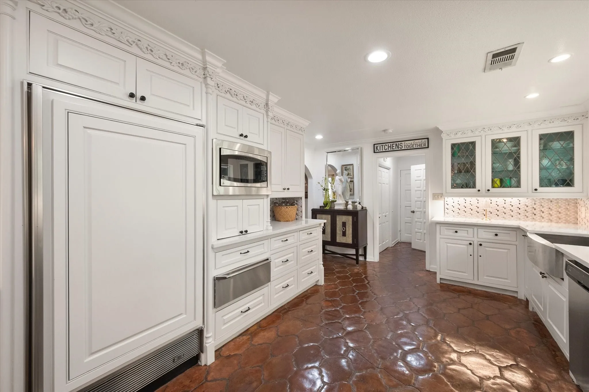 Kitchen featuring white cabinetry with ornate crown molding, integrated paneled refrigerator, stainless steel microwave, stone flooring, and solid surface countertops