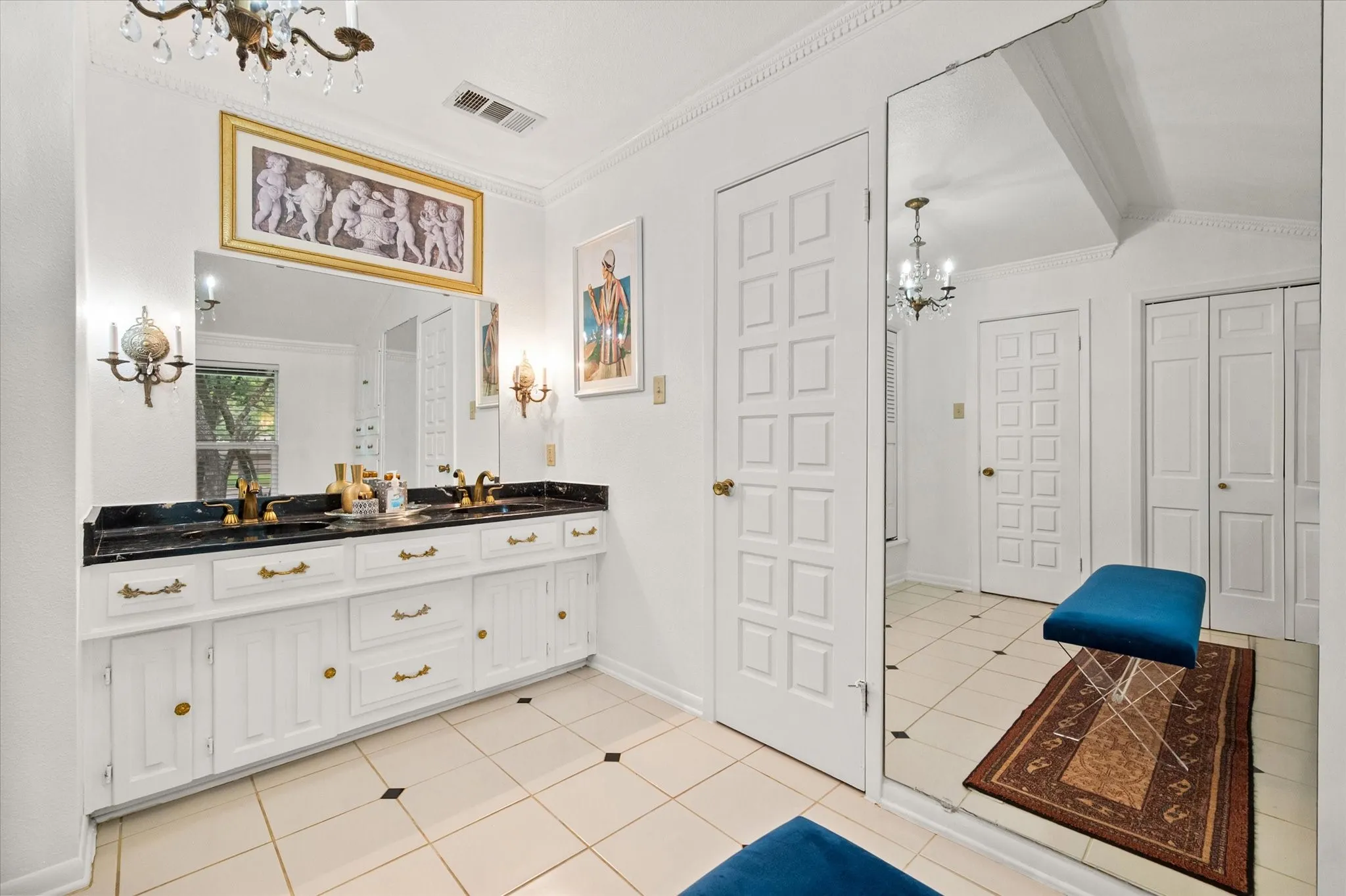 Dual vanity with black stone countertop, integrated sinks, brass-finish fixtures, and white cabinetry