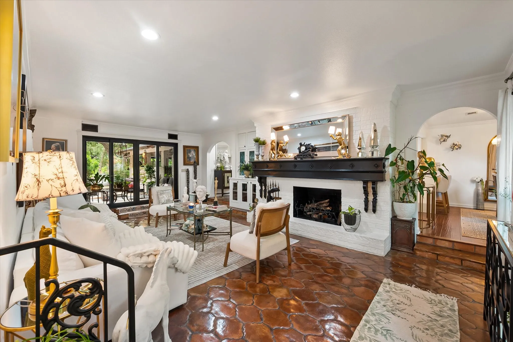 Spacious living area featuring intricate terracotta tile flooring, a white brick fireplace with a dark wood mantel, recessed lighting, and a stepped archway