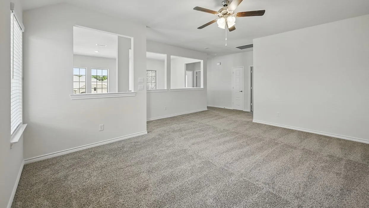 Spacious room with gray patterned carpeting, white walls, a ceiling fan with light fixture, and a window with blinds