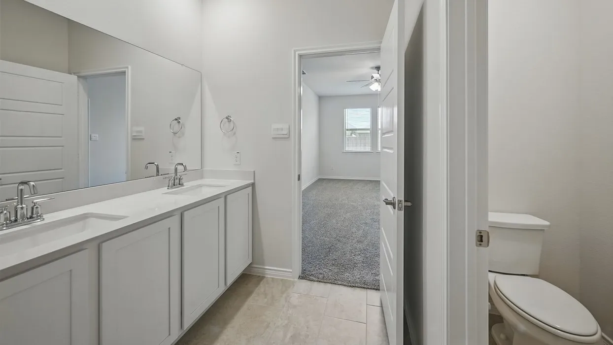 Bathroom vanity featuring dual sinks with chrome fixtures, white cabinetry, and a large wall-mounted mirror