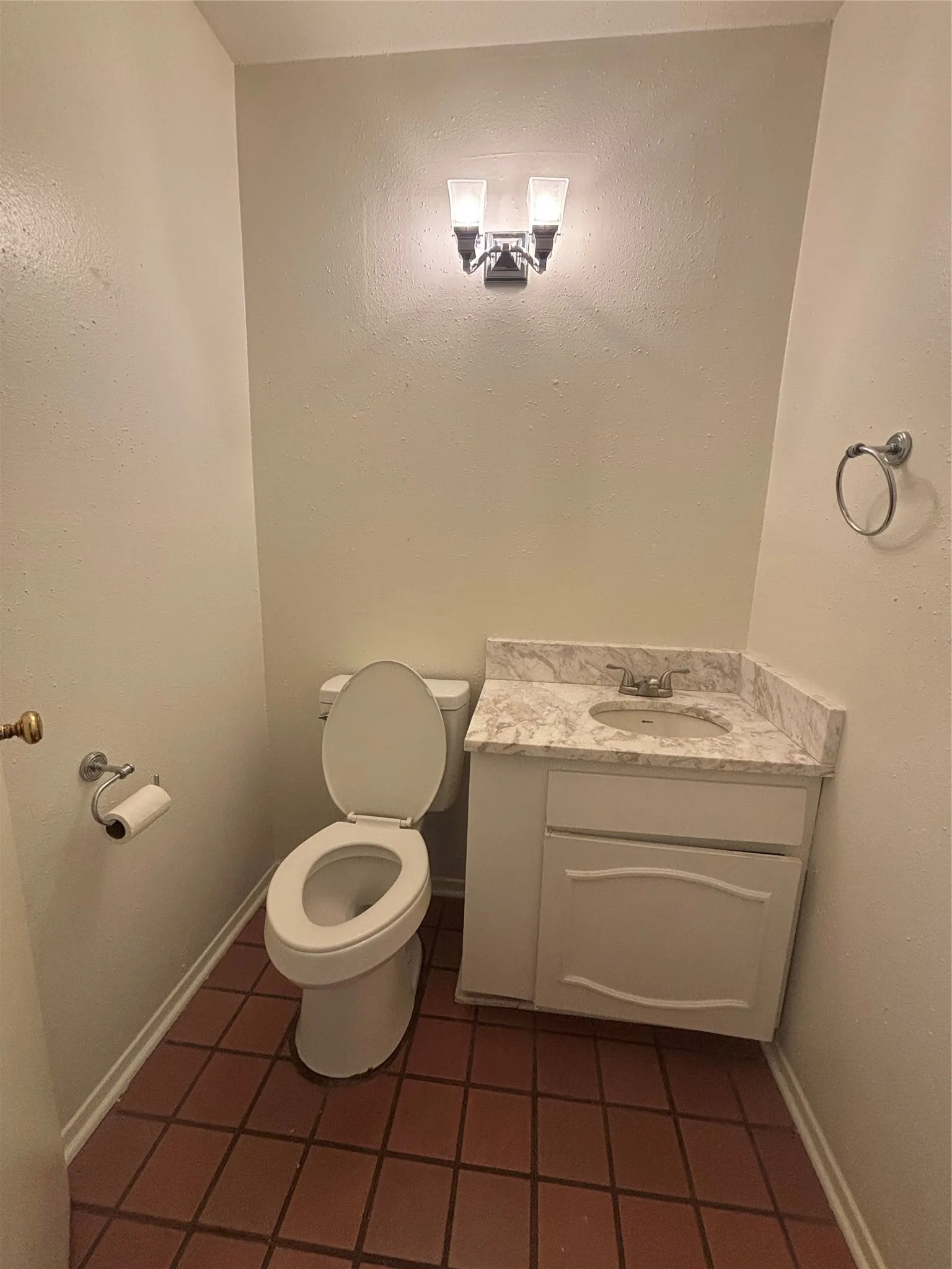 Compact powder room featuring a toilet, a single vanity with an integrated sink, a faux-marble countertop, and a white base cabinet with decorative paneling