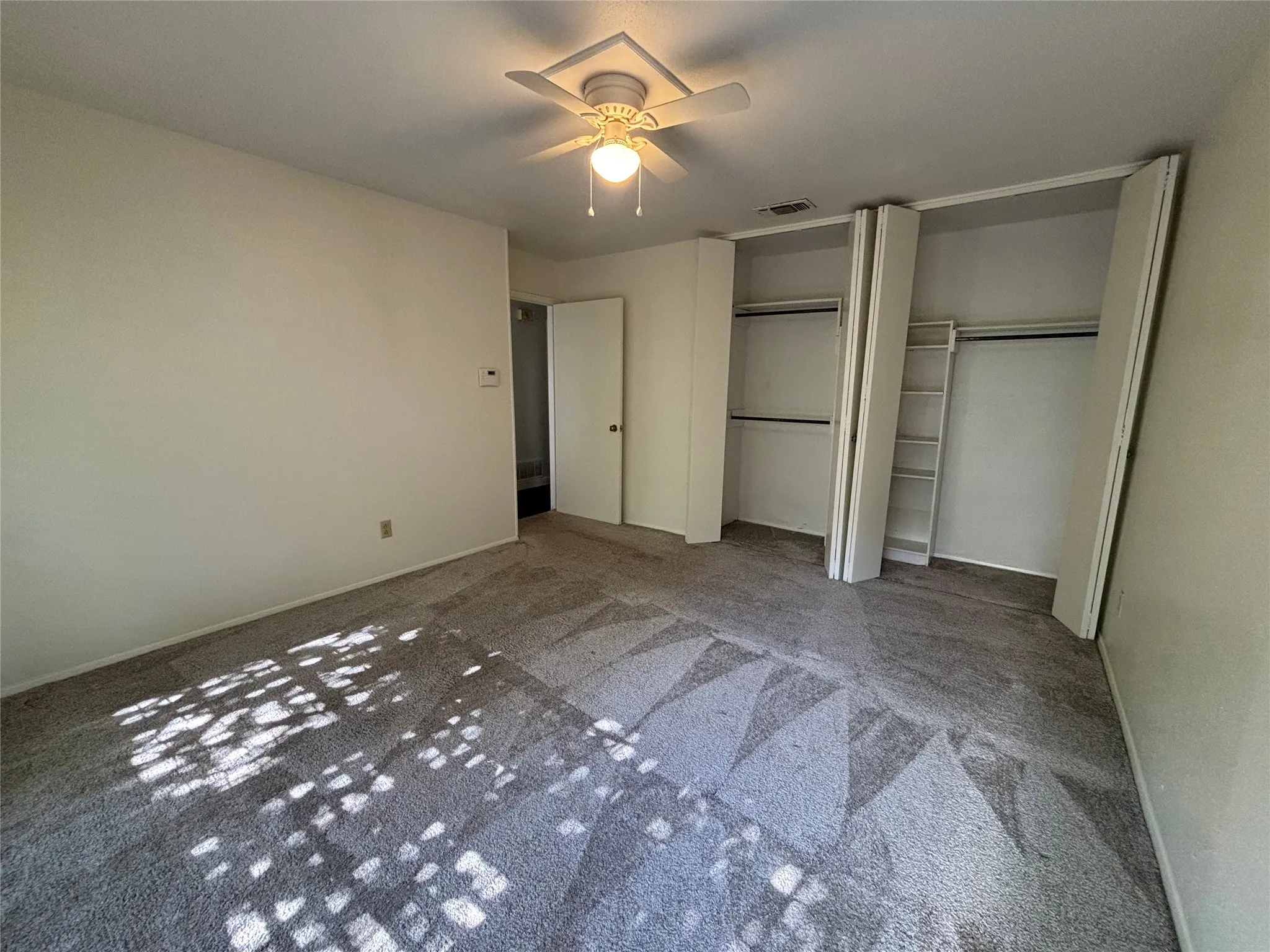 Spacious bedroom with dual closets featuring sliding glass doors, carpet flooring, and abundant natural light from multiple windows