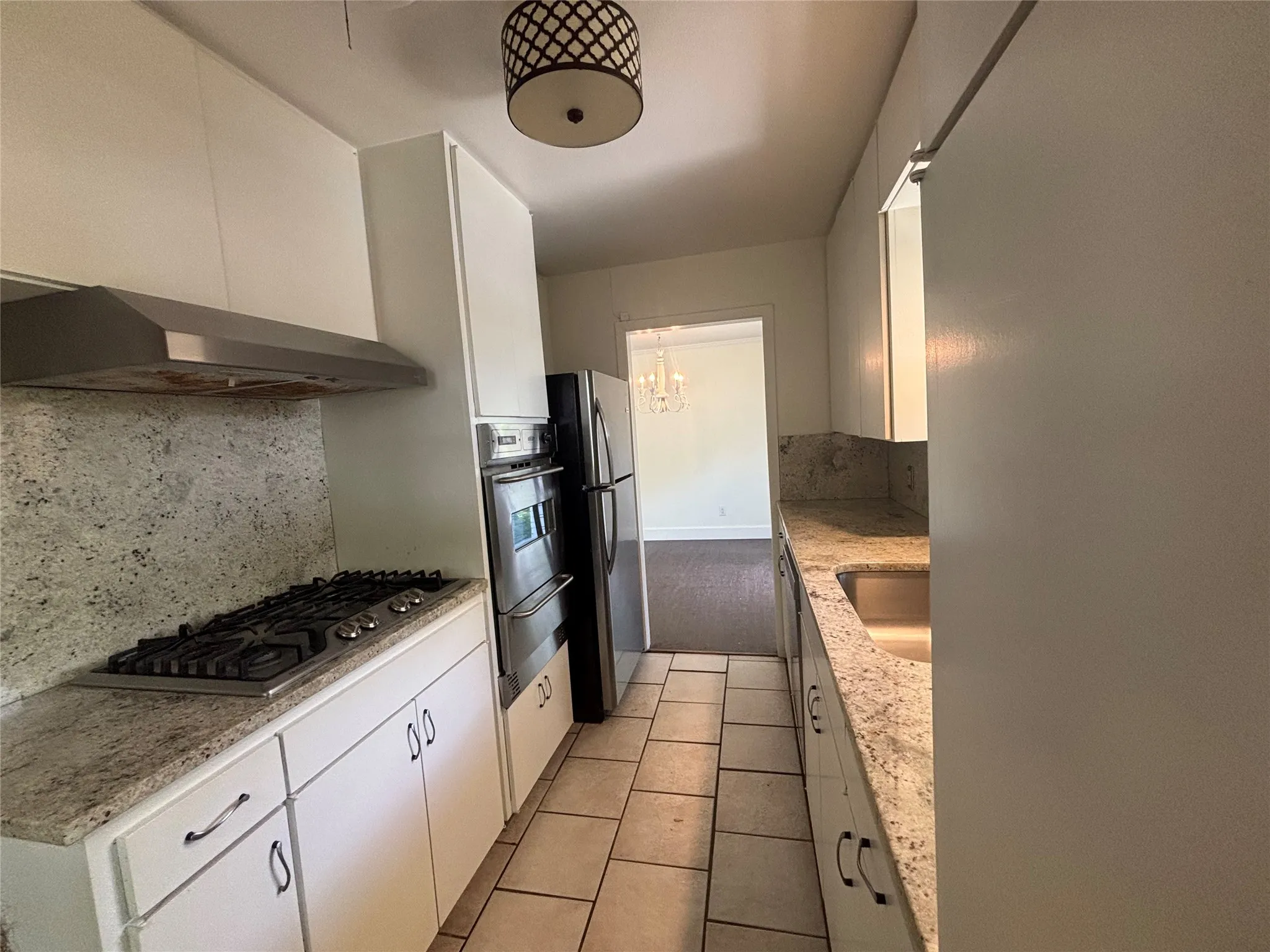 Galley kitchen featuring white cabinetry, granite countertops, tile flooring, stainless steel appliances, and a gas range with a stainless steel vent hood
