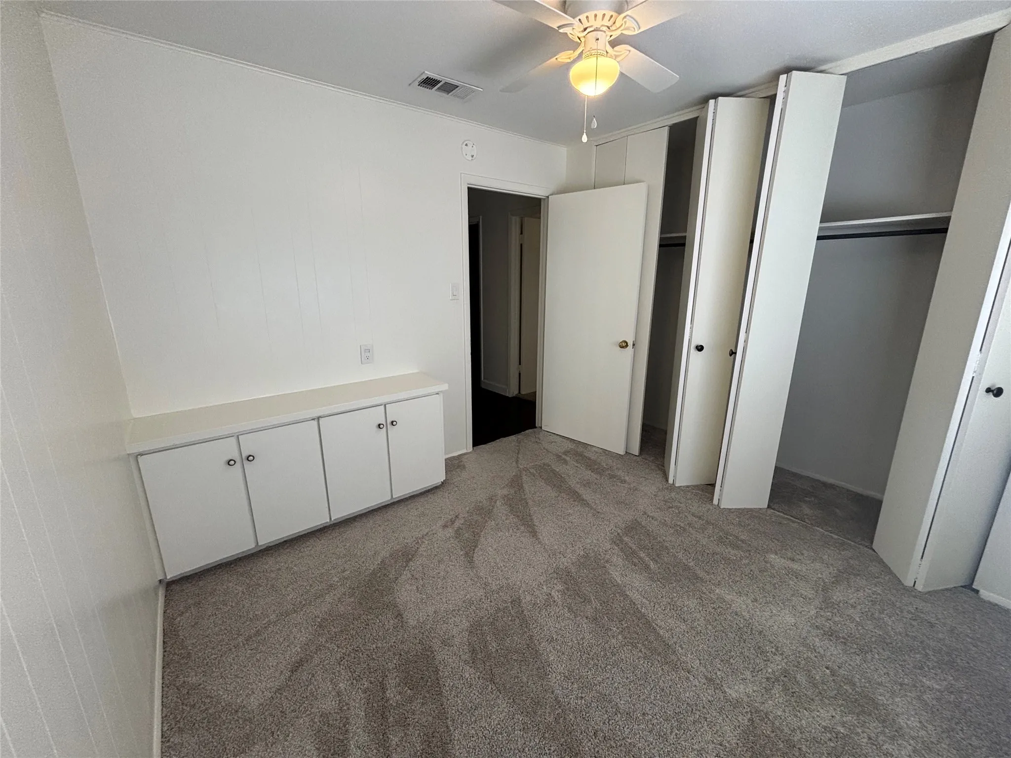 Wall-to-wall carpeting, built-in storage cabinetry, ceiling fan, and bi-fold closet doors