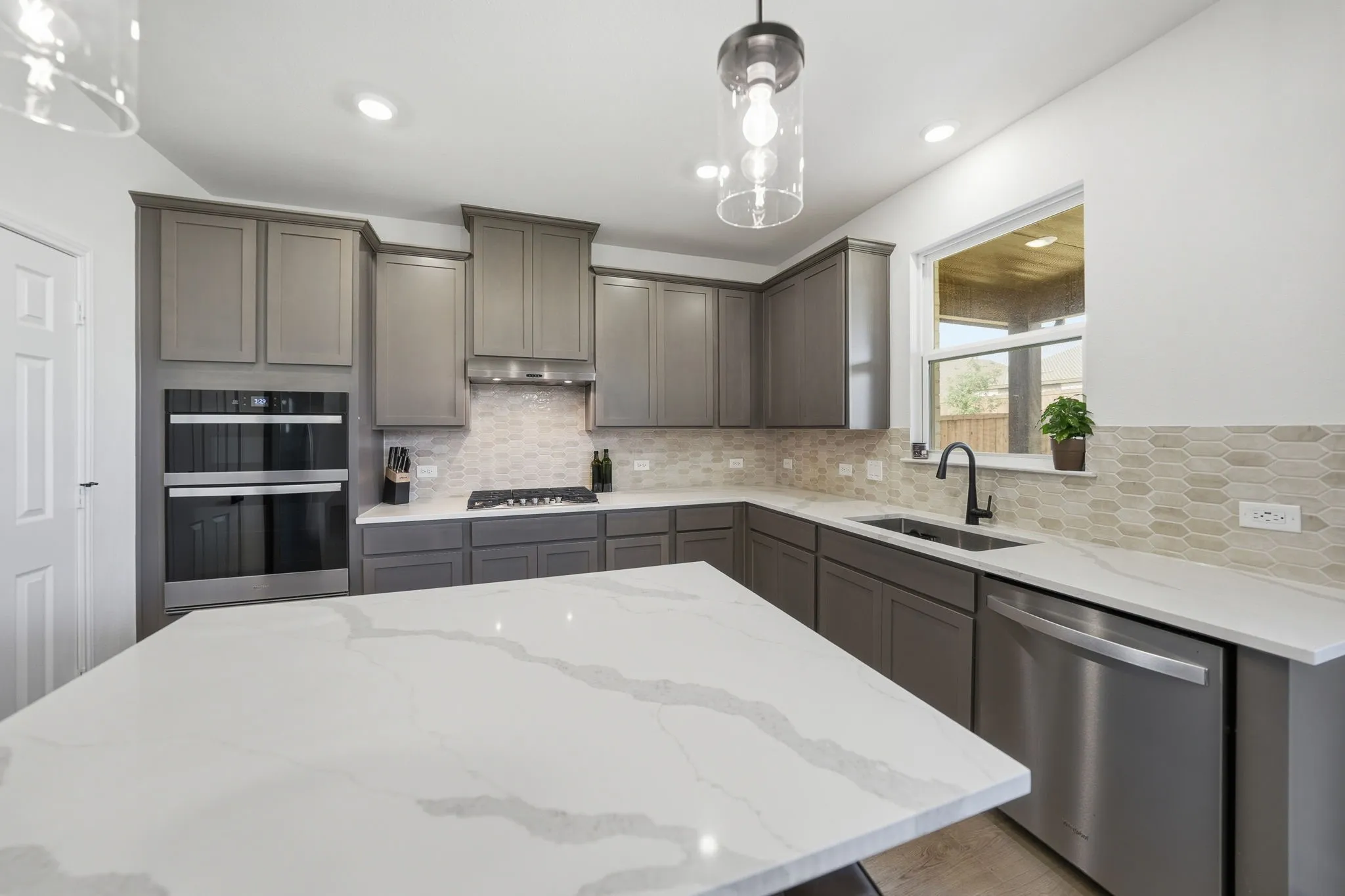 Spacious kitchen featuring an expansive island with a waterfall edge, grey cabinetry, stainless steel appliances, a geometric tile backsplash, and recessed lighting
