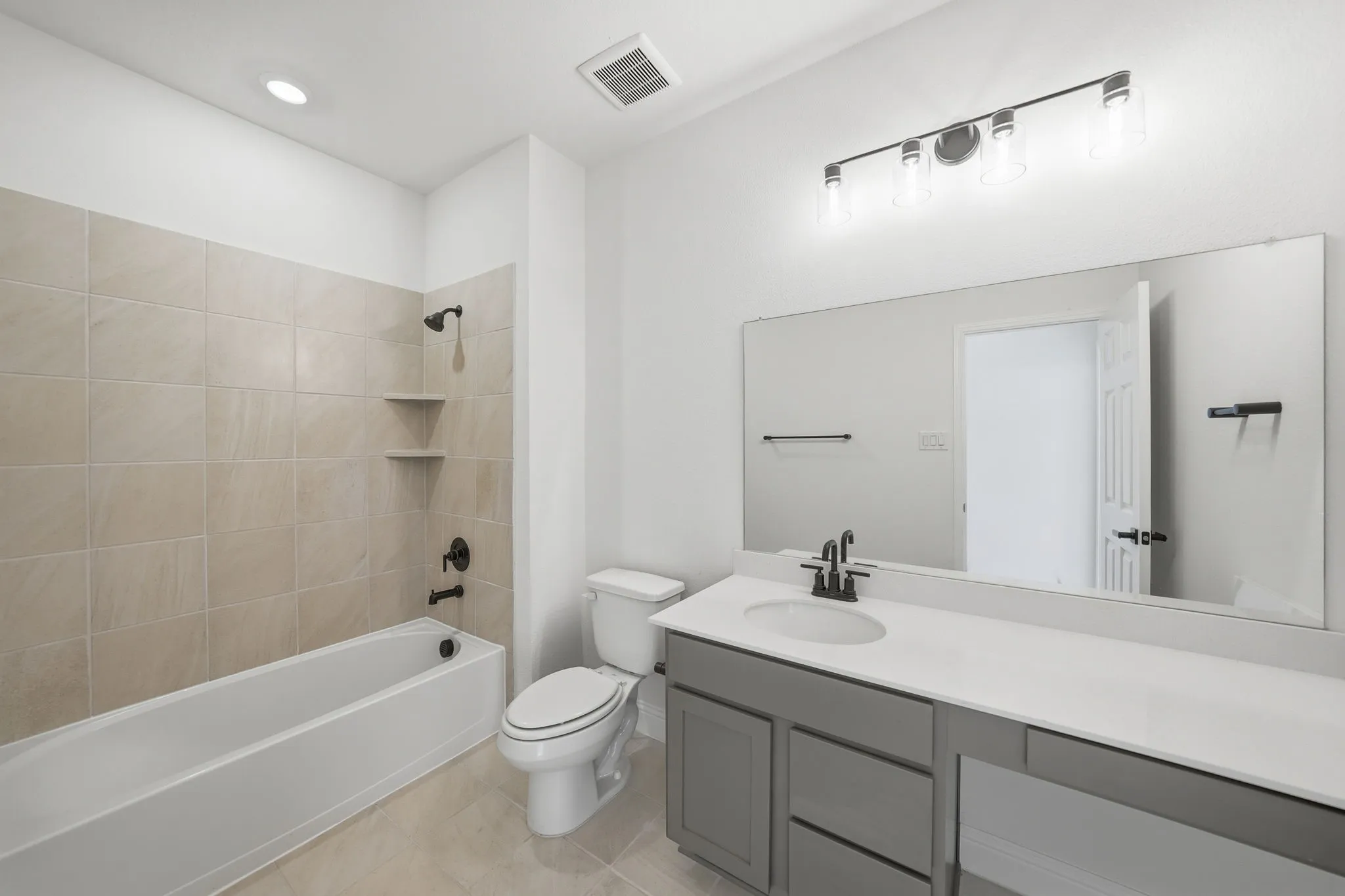 Bathroom featuring a bathtub with full-height tile surround, built-in shelving, and dark bronze fixtures