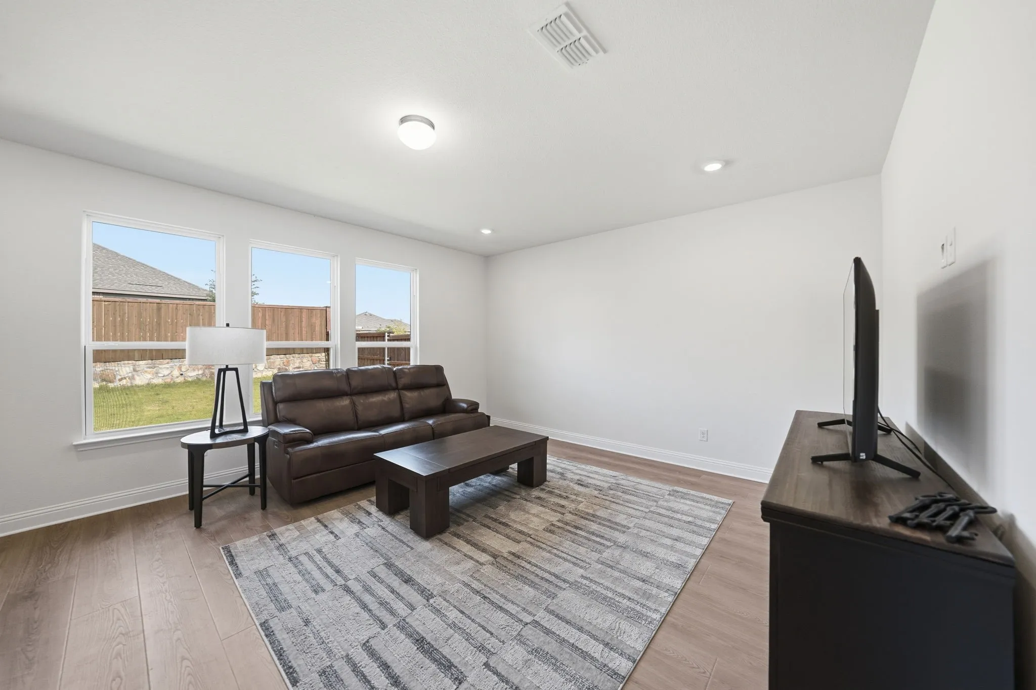 Spacious living area featuring wood-finish flooring, ample natural light from three windows, and recessed ceiling lighting