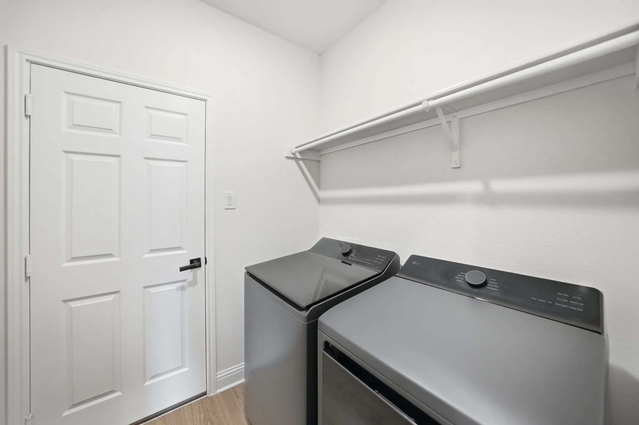 Dedicated laundry space featuring a white six-panel door, wood-finish flooring, and a white mounted shelving unit