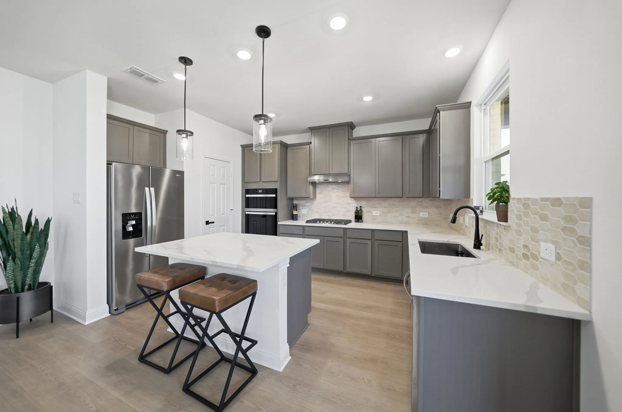 Contemporary kitchen featuring a central island with a white countertop, grey cabinetry, stainless steel appliances, a mosaic tile backsplash, and wood-finish flooring