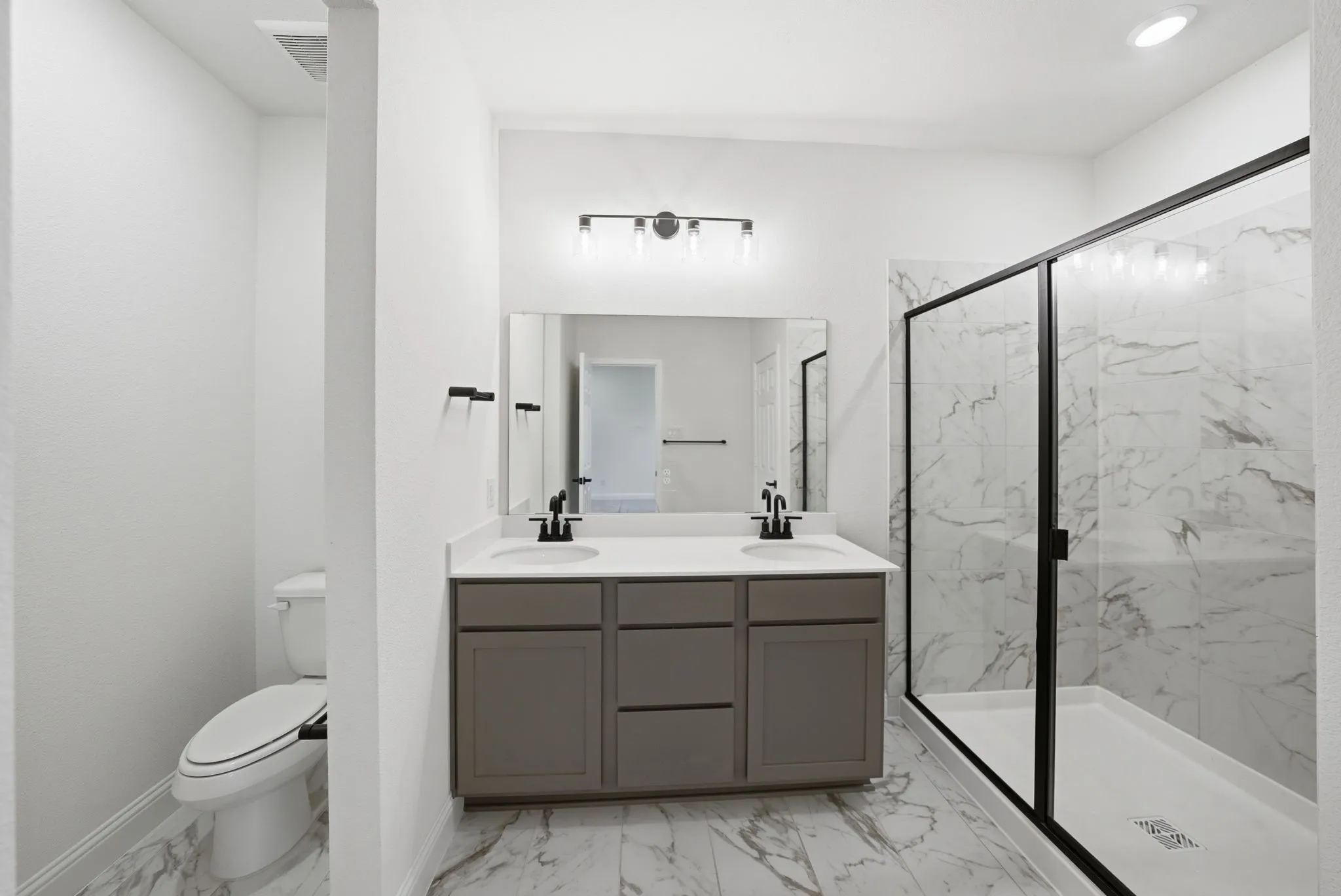 Bathroom featuring a dual vanity with a light countertop, black hardware, and an expansive glass-enclosed shower with white marbled wall tiling