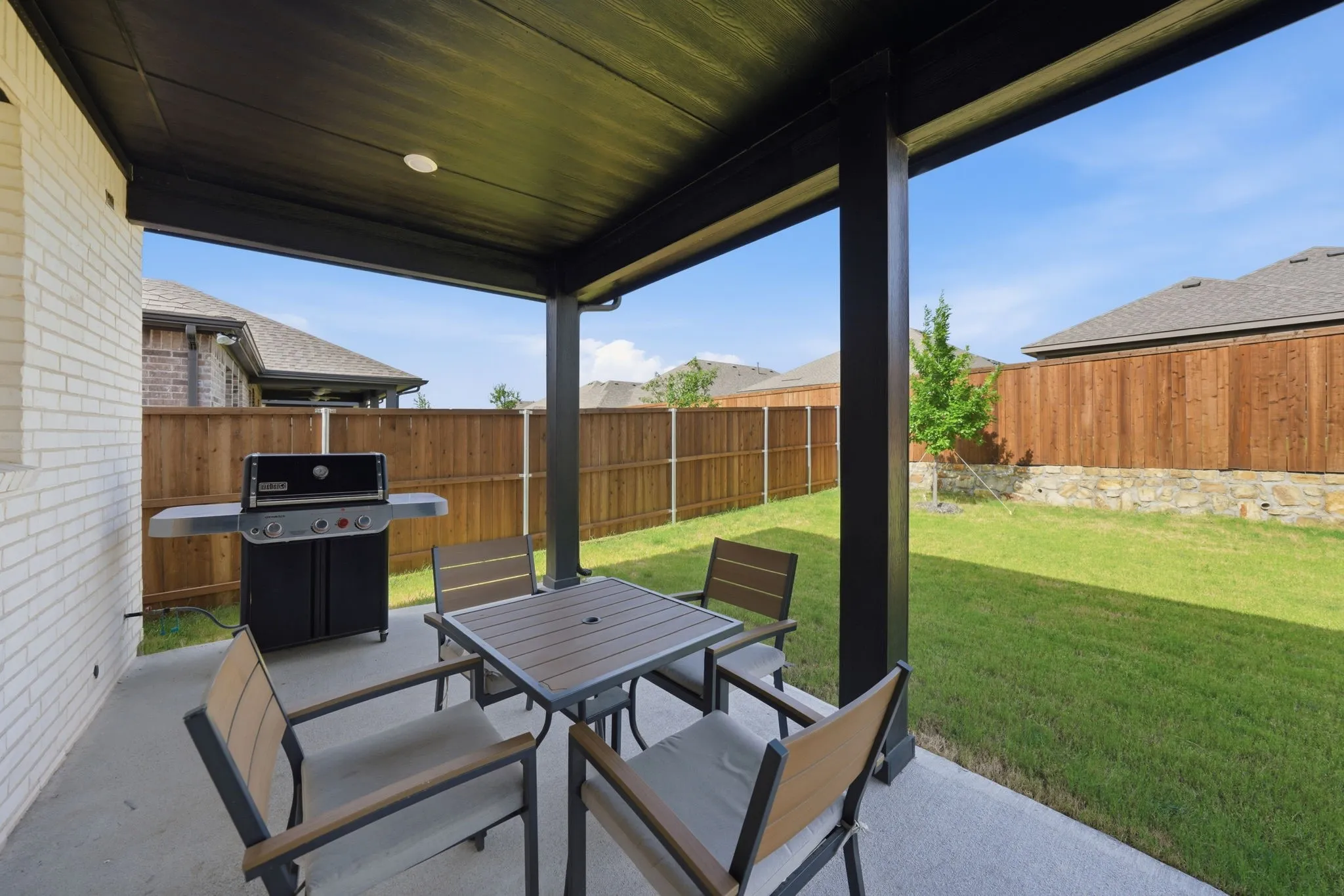 Covered concrete patio with recessed lighting, white brick exterior, and a wood privacy fence