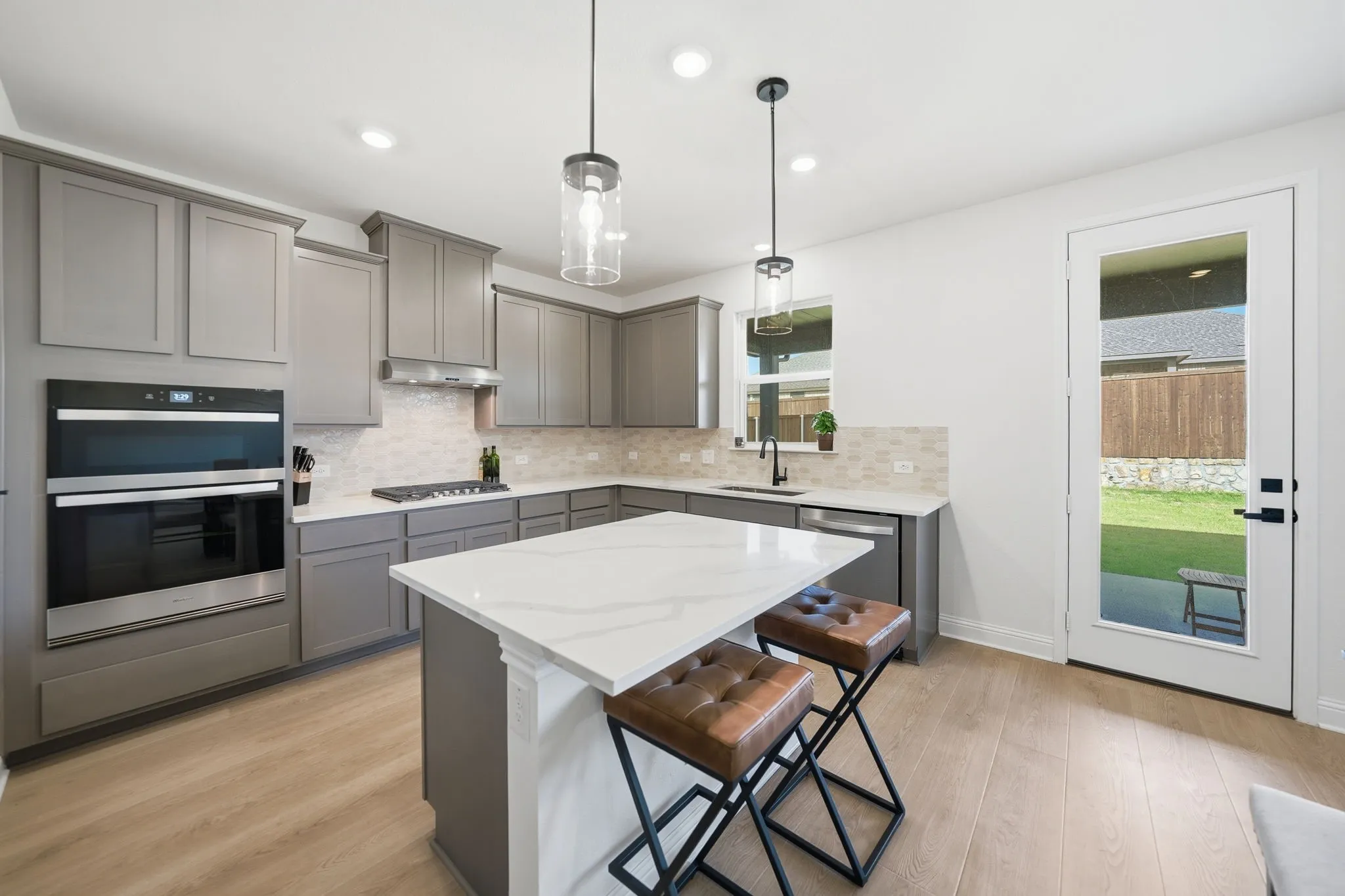Modern kitchen featuring a central island with a solid surface countertop, matte gray cabinetry, stainless steel appliances, a tile backsplash, and light wood-finish flooring