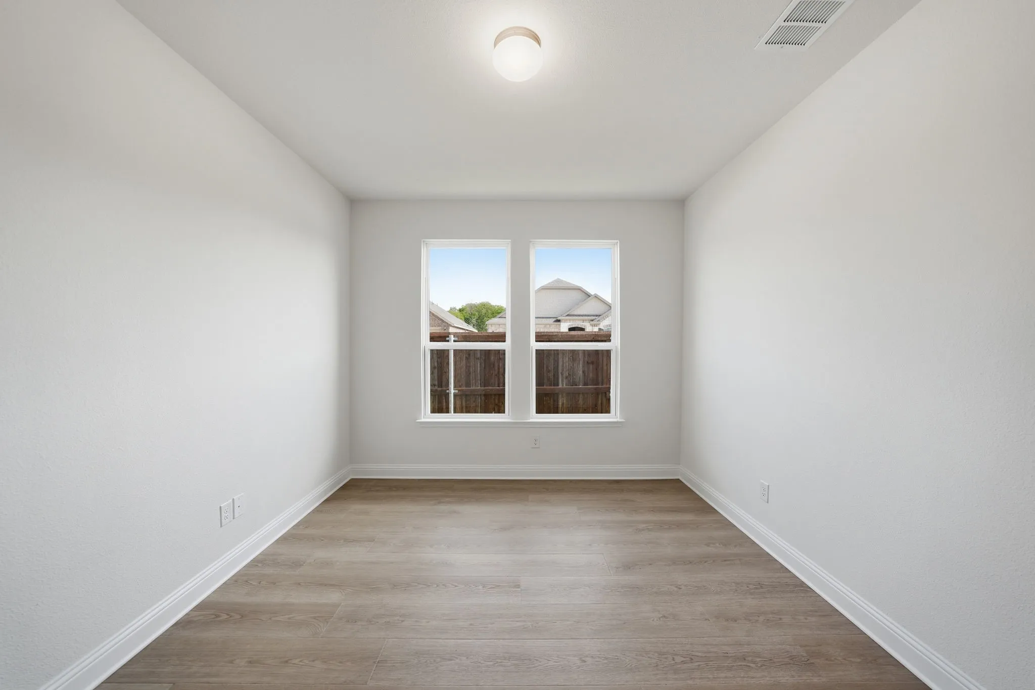 Room featuring two windows, wood-finish flooring, white baseboards, and a ceiling-mounted light fixture