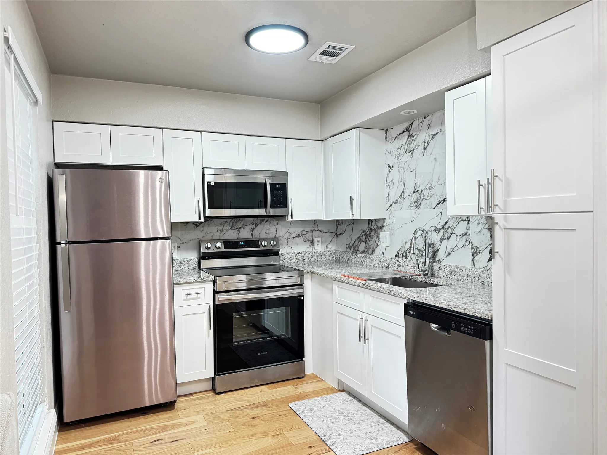 Modern kitchen featuring white shaker cabinetry, stainless steel appliances, granite countertops, and a full-height marble-patterned backsplash