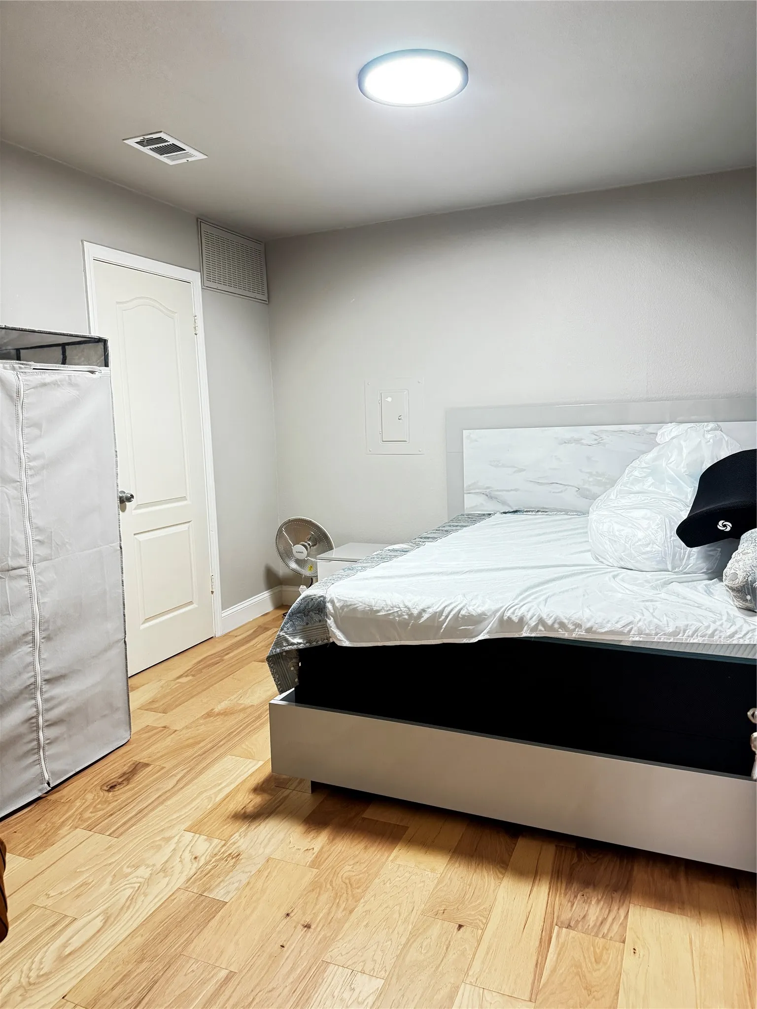 Hardwood flooring complements a neutral wall palette in this room featuring a ceiling-mounted light fixture, white door with panel detailing, and baseboard trim