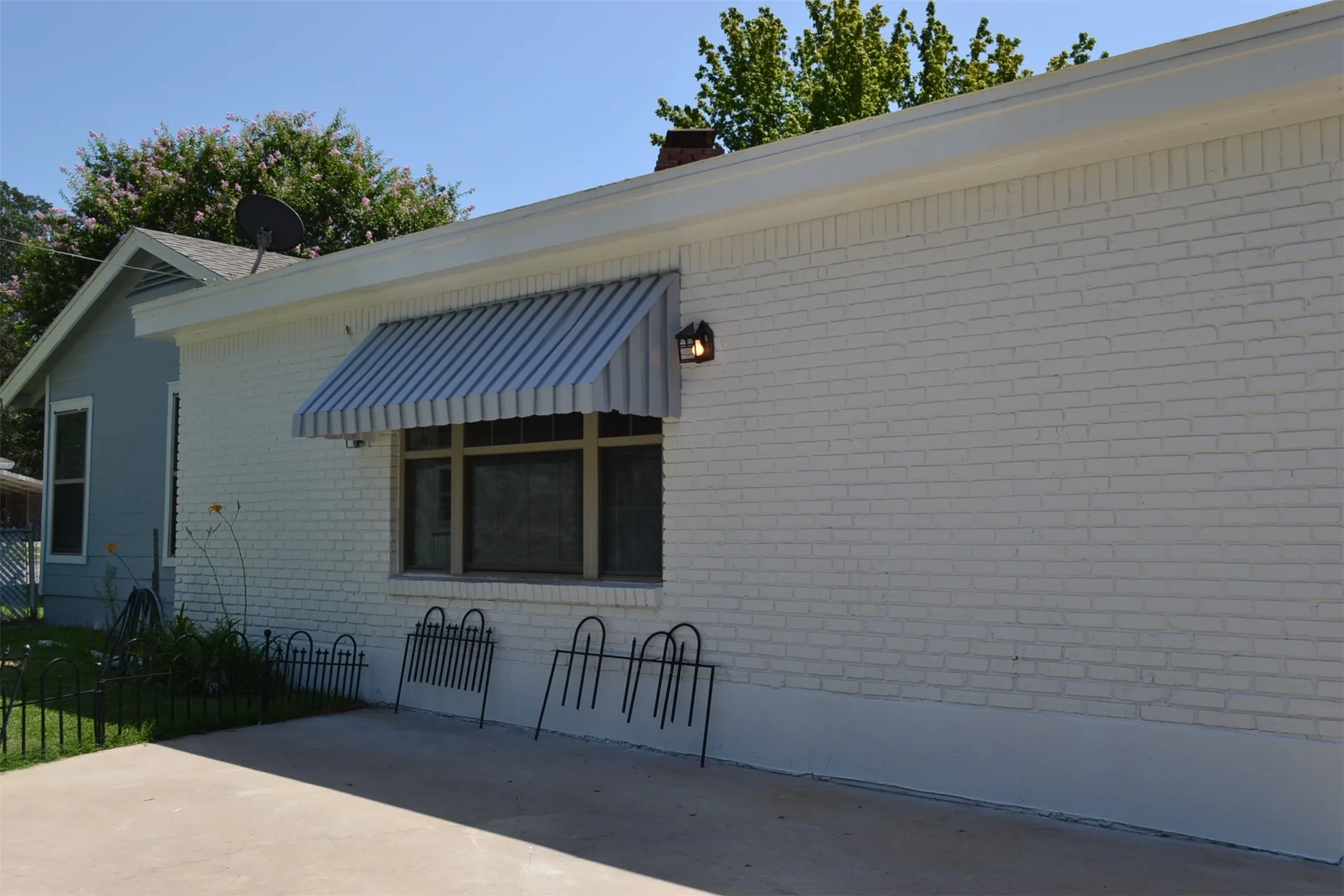 White painted brick exterior featuring a striped window awning, an outdoor wall light fixture, and a concrete patio space