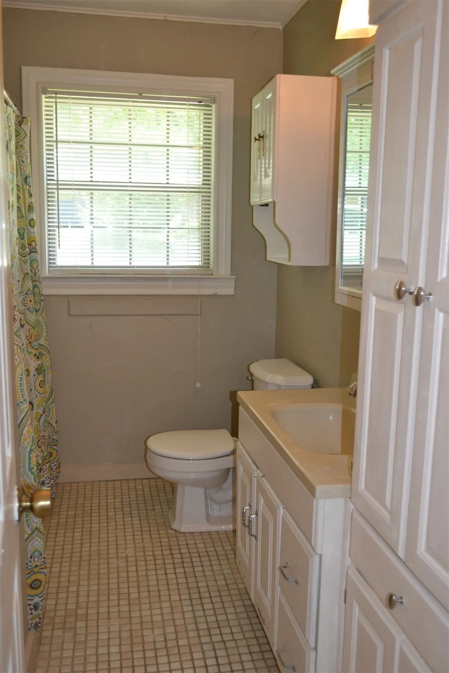 Bathroom featuring a white vanity with integrated sink, white cabinetry, a built-in toilet, and a window with blinds