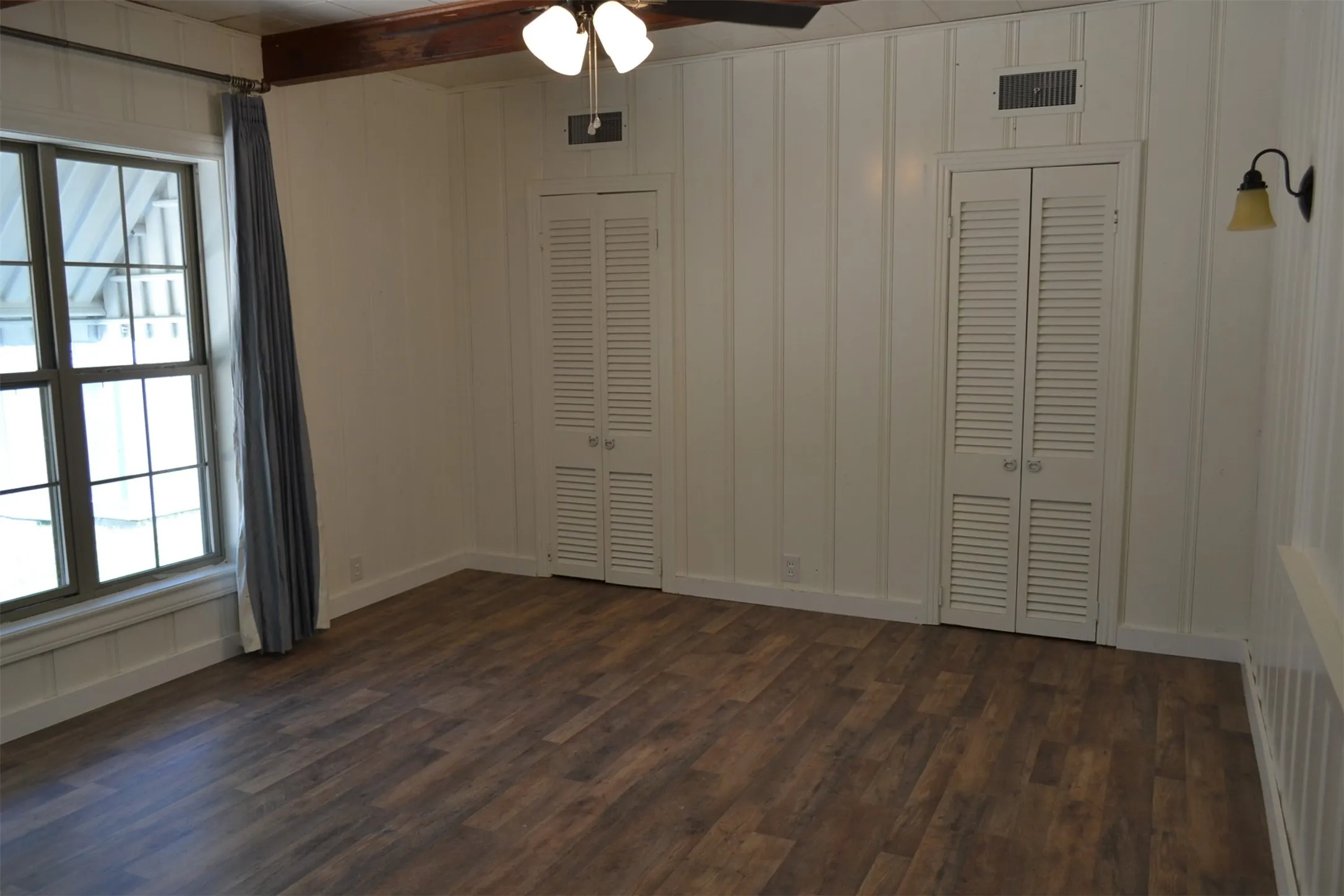 Spacious room featuring wood-finish flooring, vertical paneling, and two louvered bifold closet doors