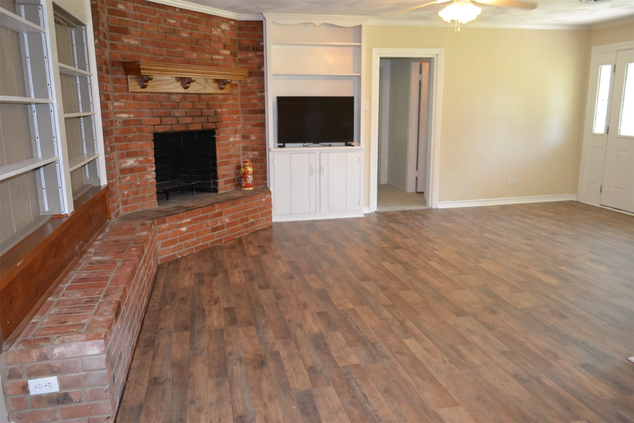 Living area featuring wood-finish flooring, a brick fireplace with a carved wood mantel, and built-in shelving with cabinetry
