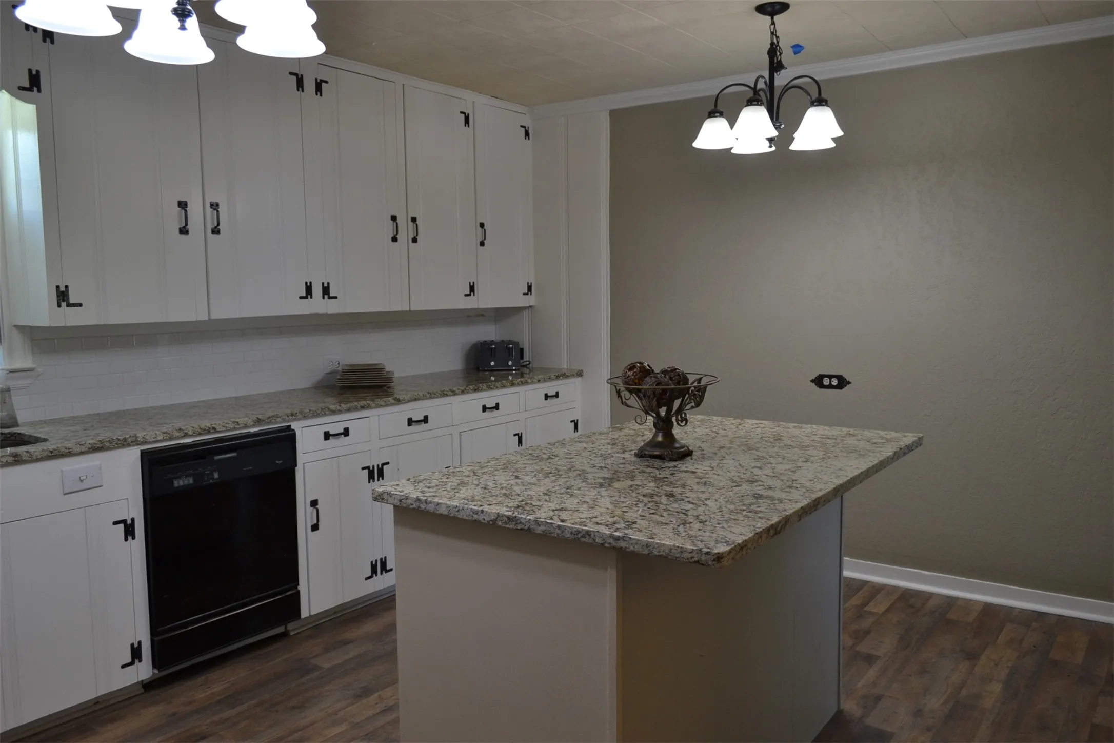 Kitchen featuring white cabinetry with dark hardware, granite countertops, a built-in dishwasher, an island with granite countertop, and wood-finish flooring