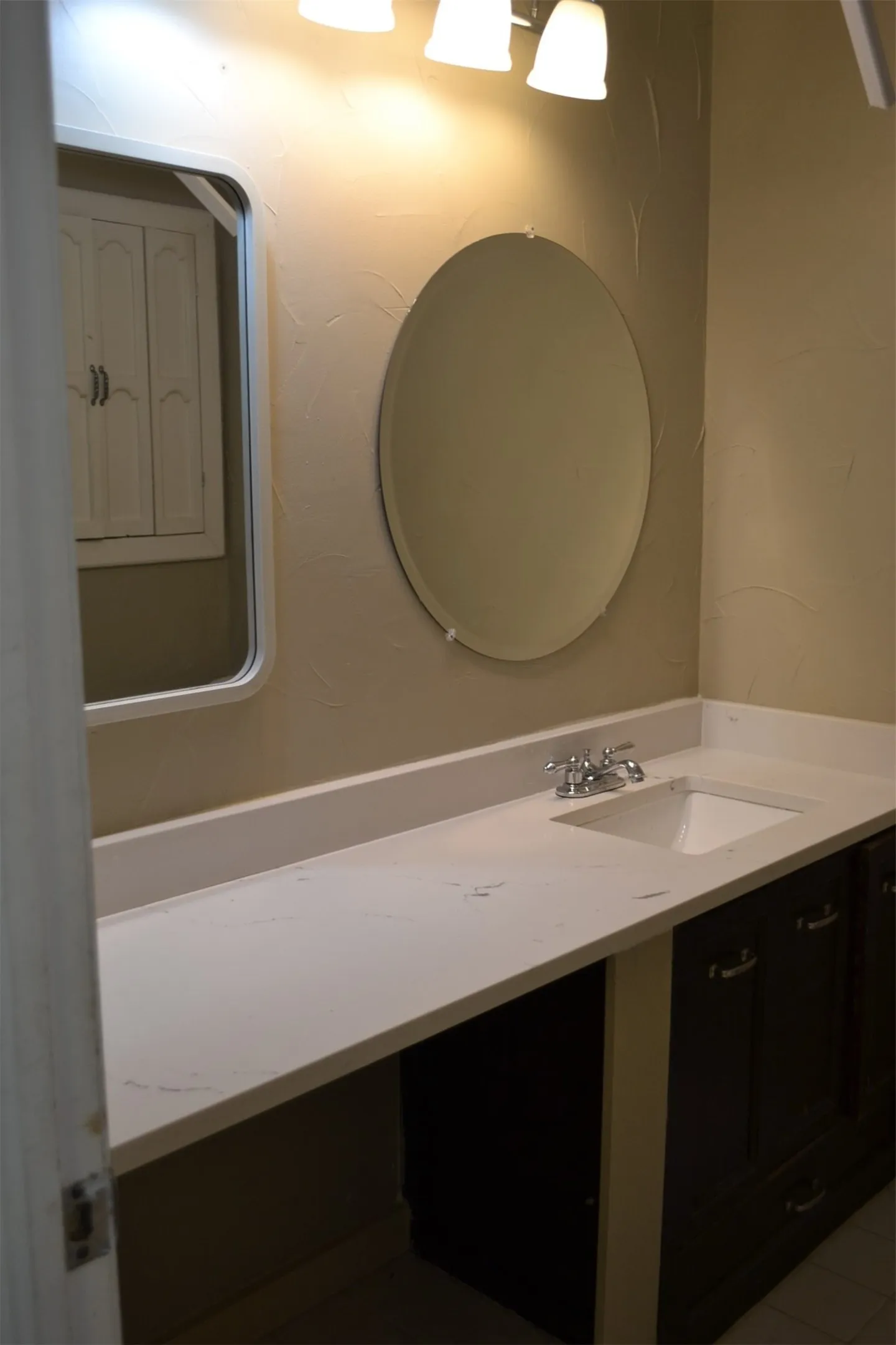 Bathroom vanity featuring an integrated sink, polished chrome faucet, white countertop, and dark wood-finish cabinetry