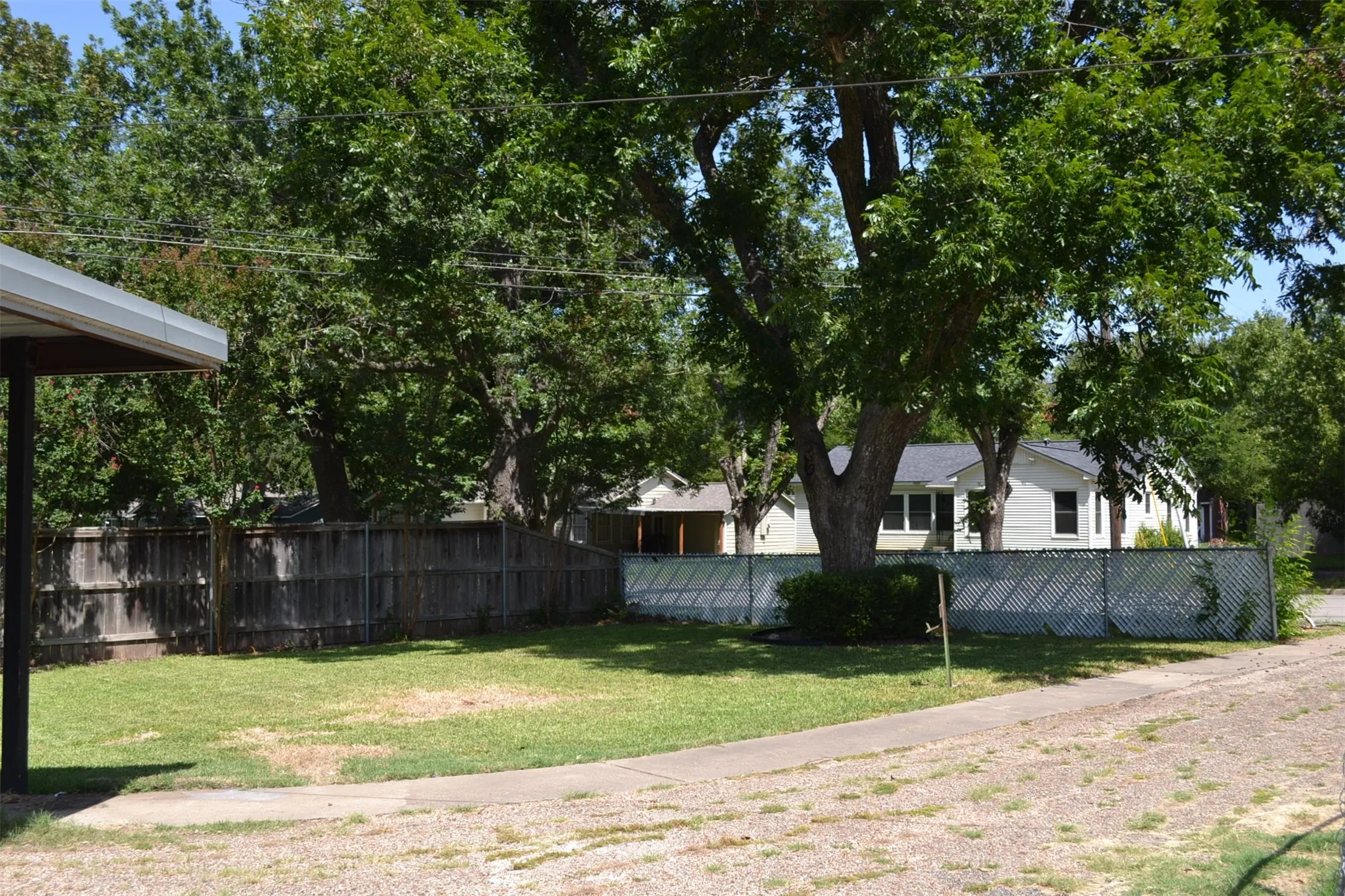 Expansive lot featuring mature shade trees, a grass lawn, and a wood privacy fence
