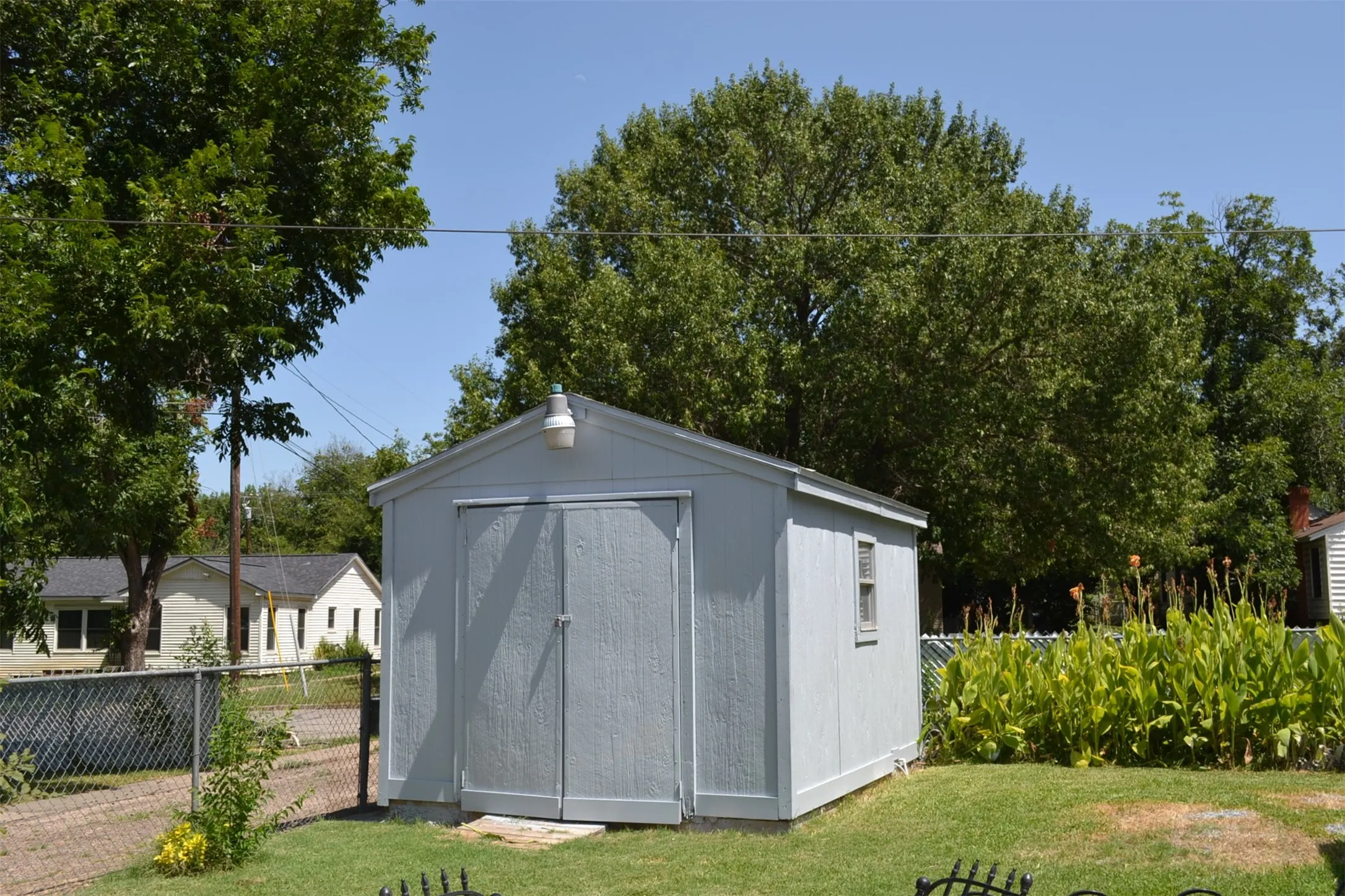 Gable-roof storage shed featuring light blue siding, double doors, a side window, and an exterior light fixture