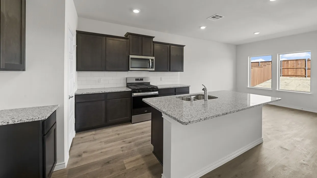 Kitchen featuring dark wood-finish cabinetry, granite countertops, subway tile backsplash, and stainless steel appliances