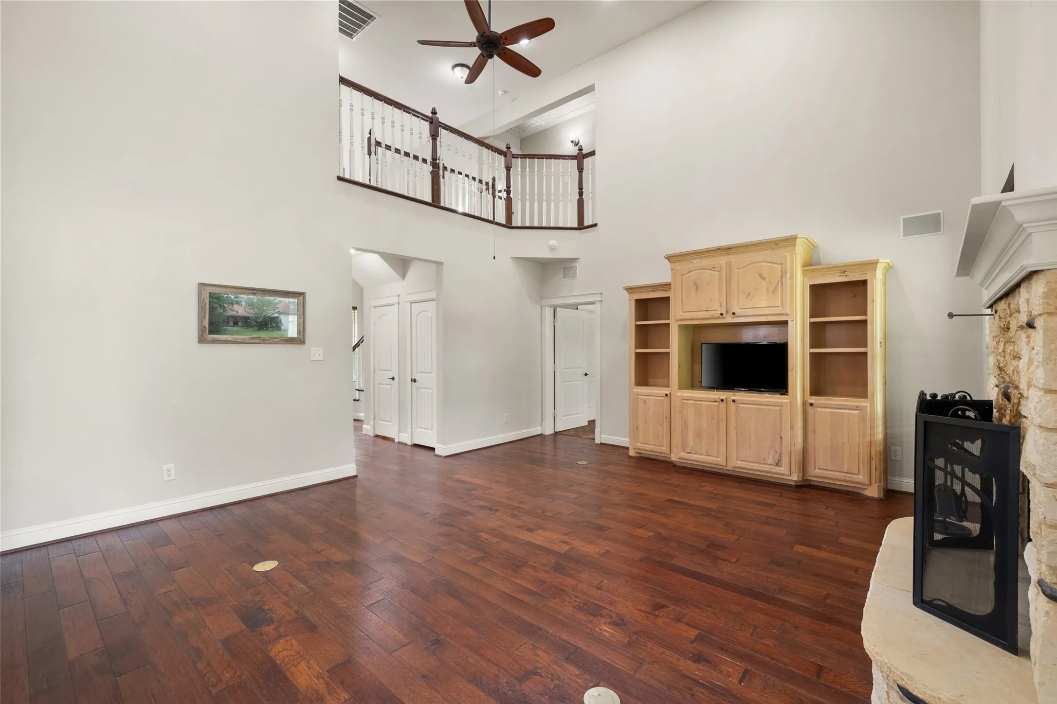 Open living room with hardwood floors, soaring ceiling, built-in entertainment center and second-floor balcony views.
