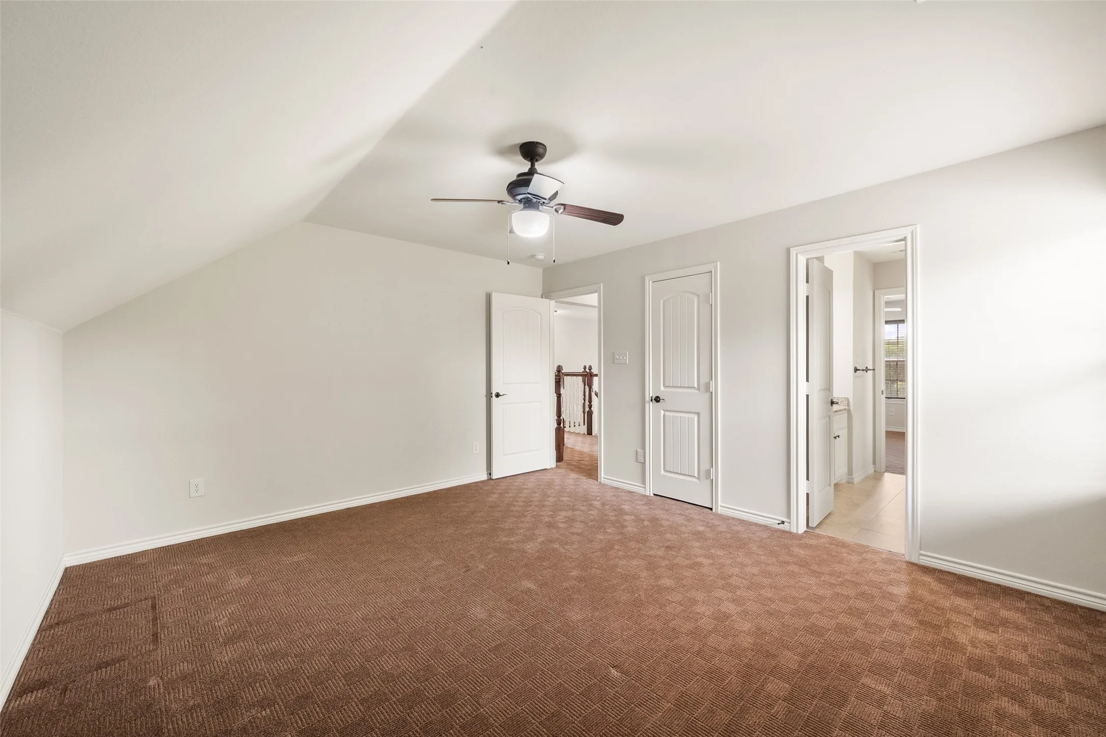 Generously sized upstairs bedroom with vaulted ceiling, ceiling fan and access to a shared bathroom.