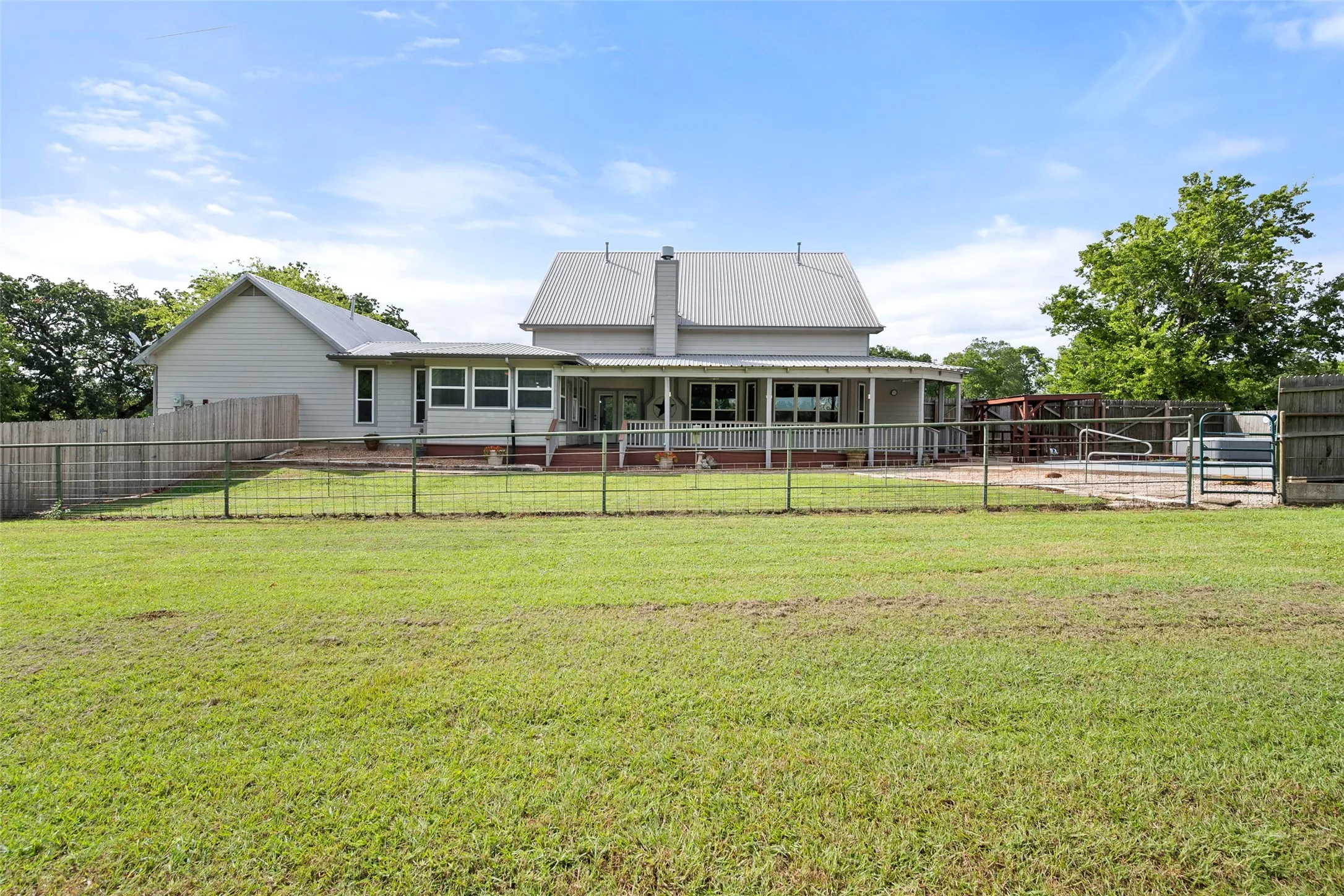 Rear view of the Streetman acreage property highlighting the fenced yard, covered porch, pool area and expansive lawn.