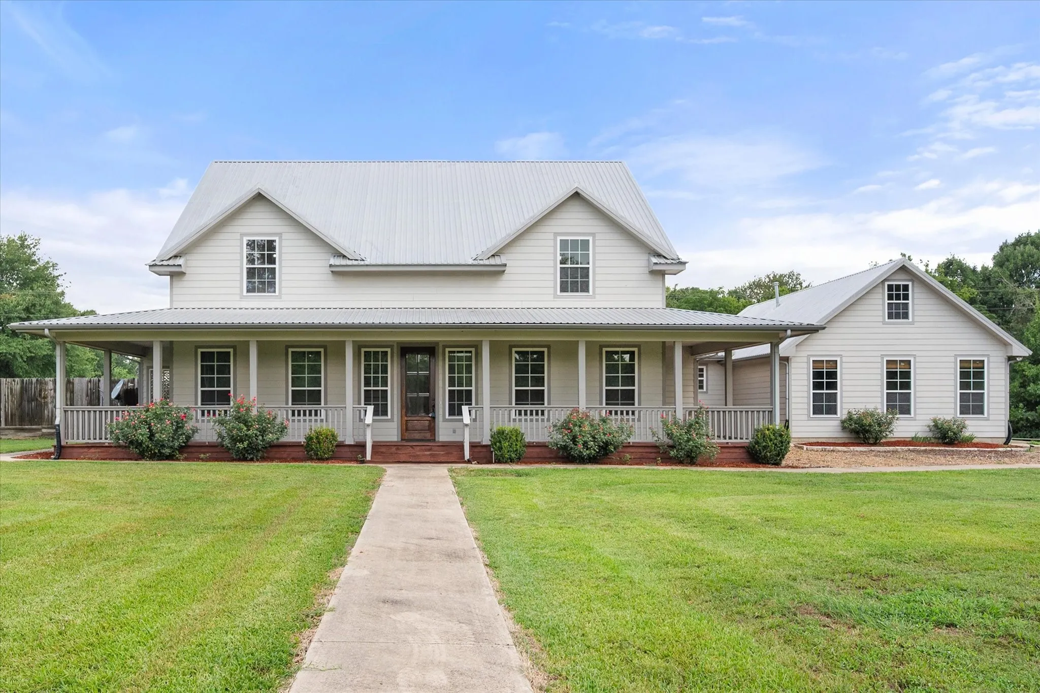 Front exterior of the 17.91-acre Streetman farmhouse with wraparound porch, landscaped grounds and attached three-car garage.