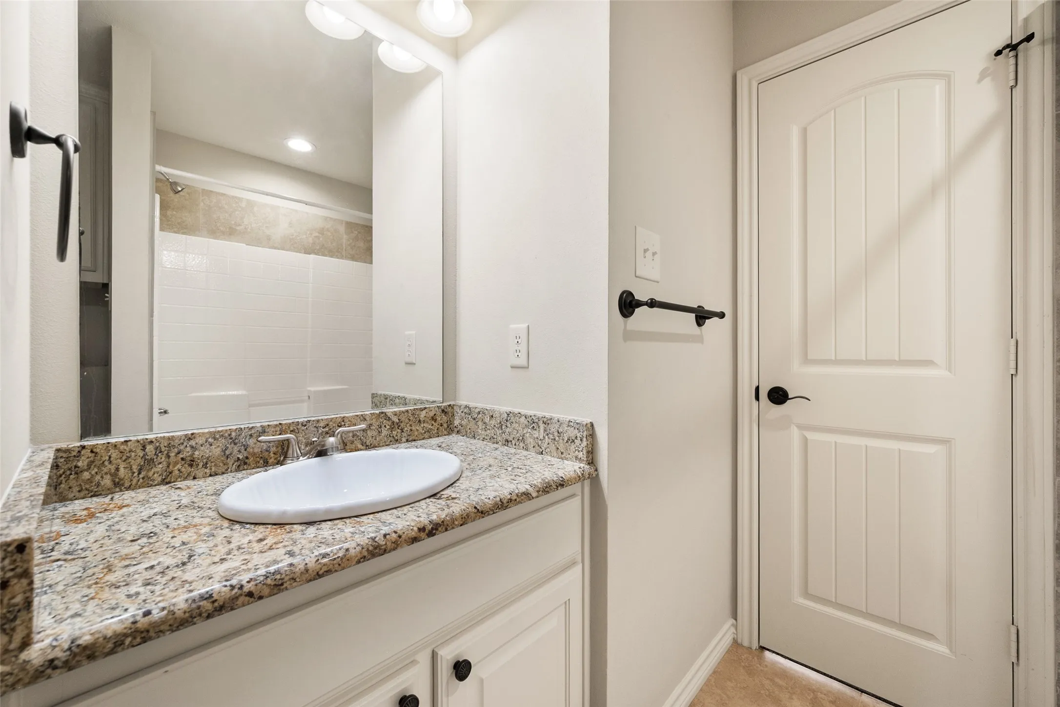 Upstairs ensuite Jack-and-Jill bathroom with granite vanity, tiled tub and shower combination and built-in storage.