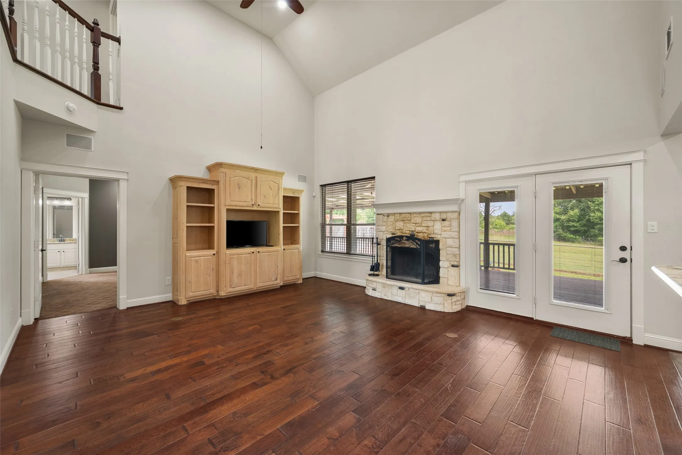 Spacious living area featuring a raised stone fireplace, hardwood flooring and French doors to the backyard.