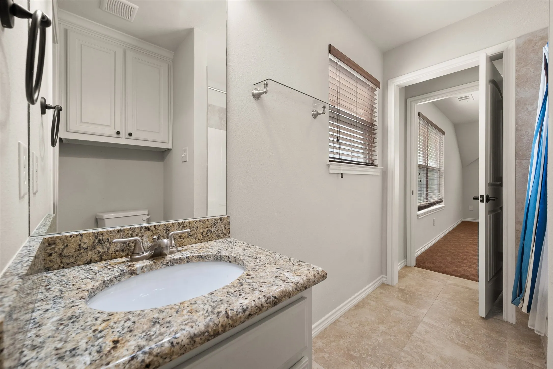 Upstairs second primary bathroom with granite vanity, built-in cabinetry, tiled flooring and ample natural light.