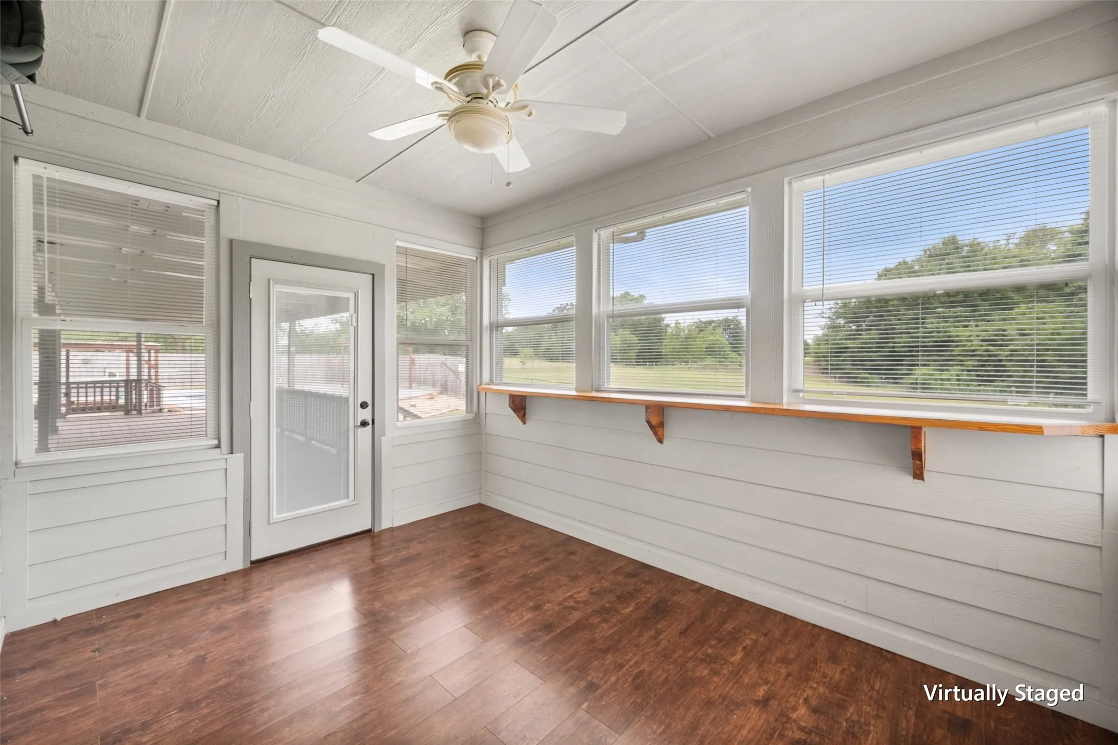 Bright sunroom with walls of windows, backyard views, hardwood flooring and direct outdoor access.