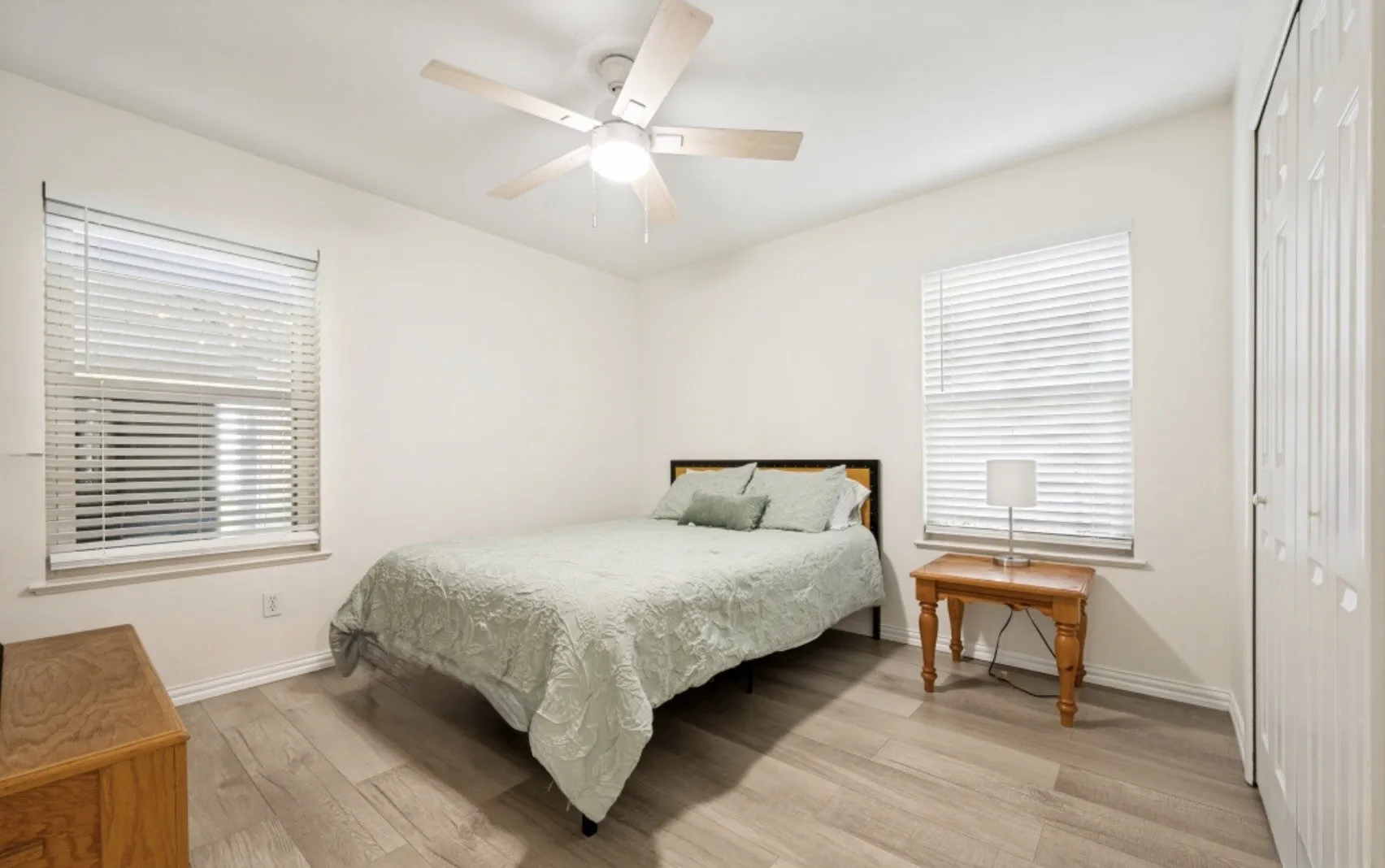 Room featuring light wood-finish flooring, a ceiling fan with integrated lighting, two windows with horizontal blinds, and a bifold closet door