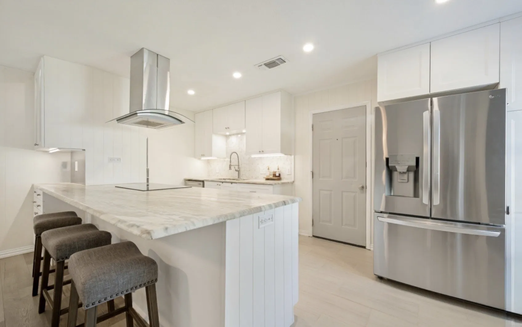 Contemporary kitchen featuring an expansive island with a light-toned countertop, white cabinetry, a stainless steel refrigerator, and recessed lighting