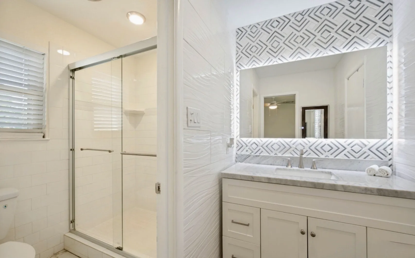 Bathroom featuring a custom vanity with undermount sink, a marble countertop, and an illuminated mirror with a tiled surround