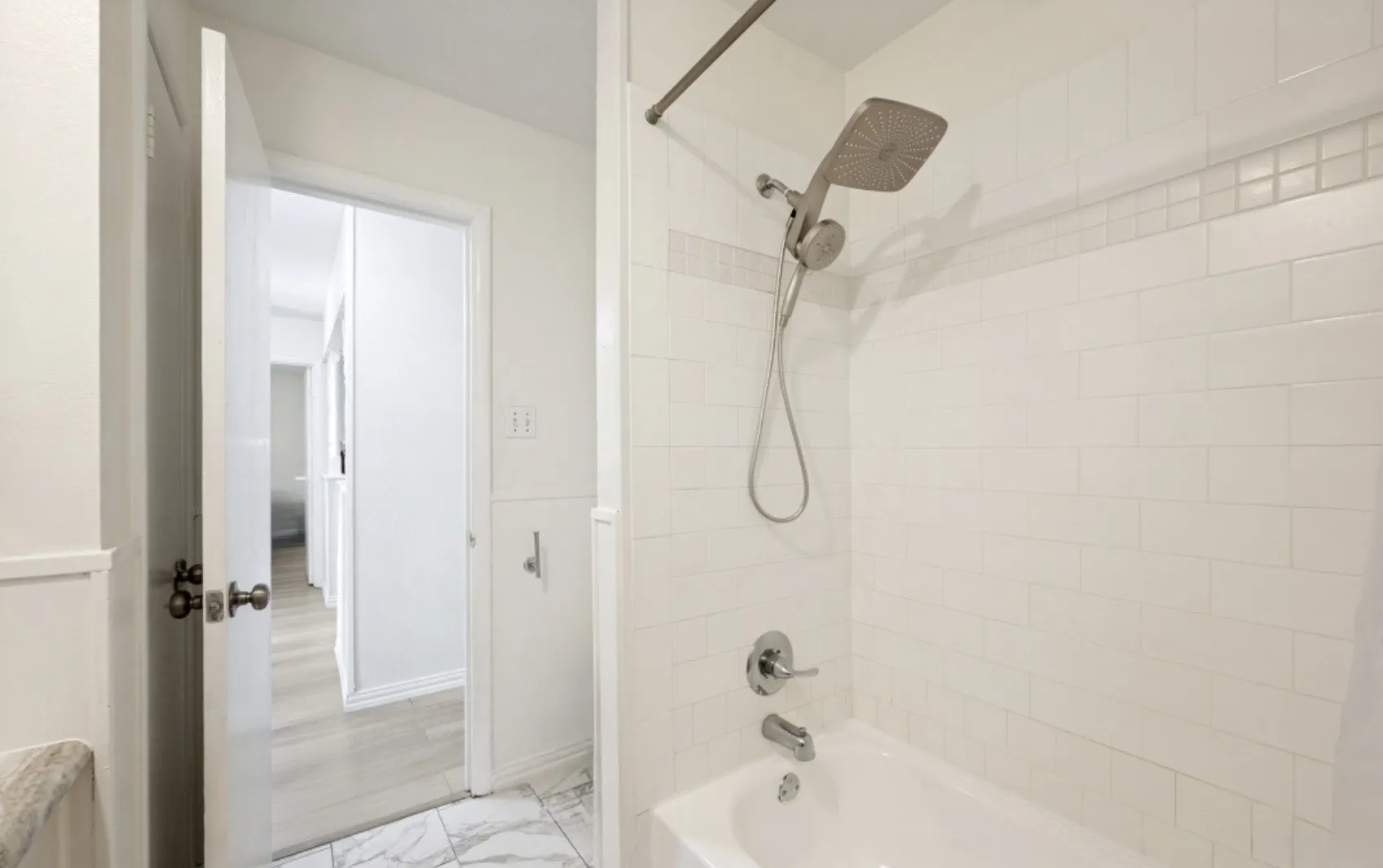 Bathtub and shower combination featuring subway tile surround with a decorative accent band and a brushed nickel showerhead