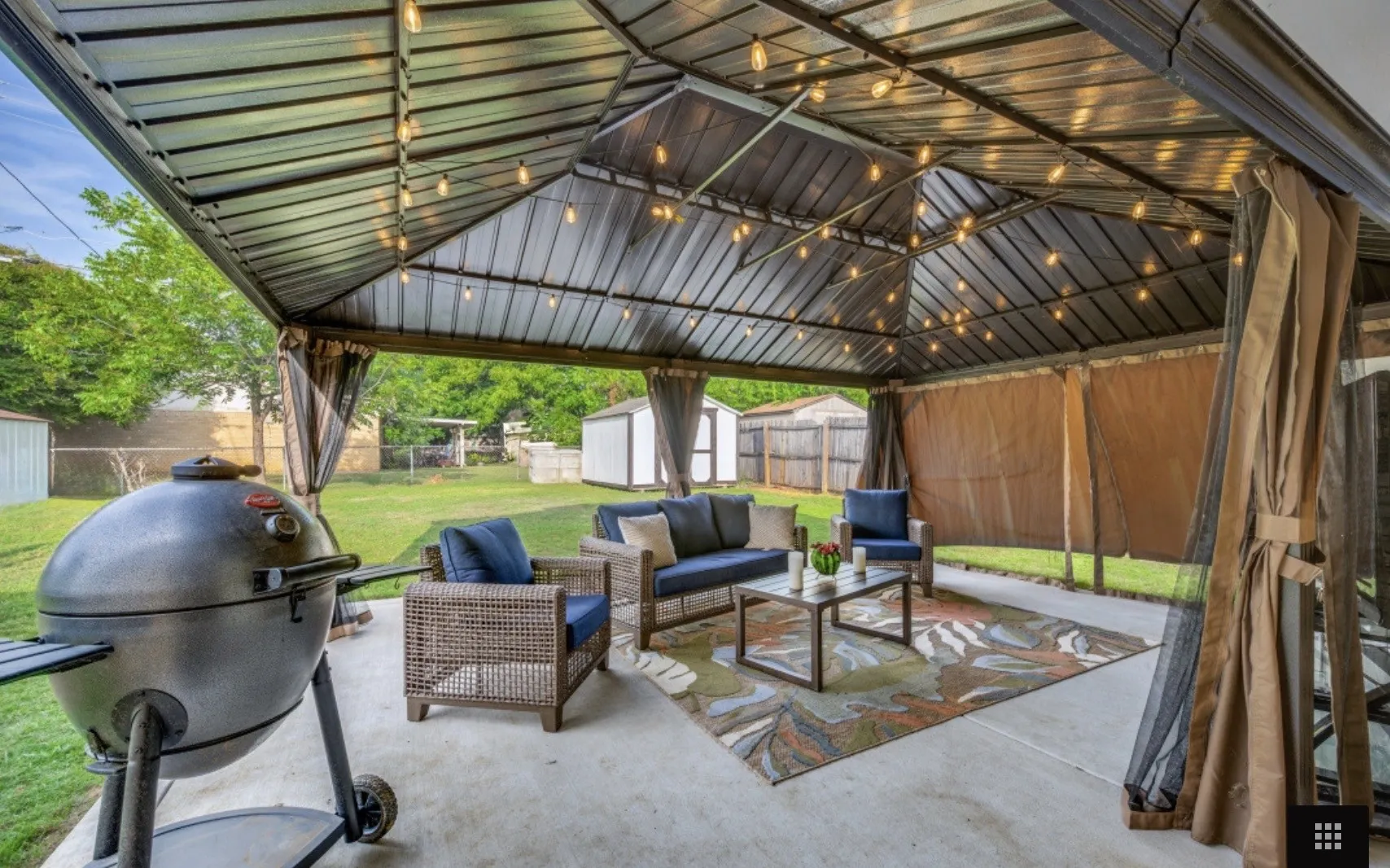 Expansive outdoor patio featuring a covered gazebo with string lighting, concrete flooring, and privacy curtains