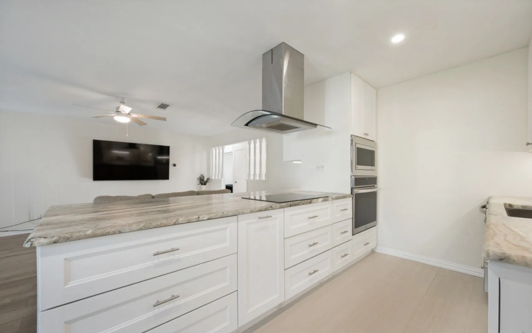 Kitchen island featuring a light-toned countertop, integrated cooktop, and white cabinetry with brushed nickel hardware