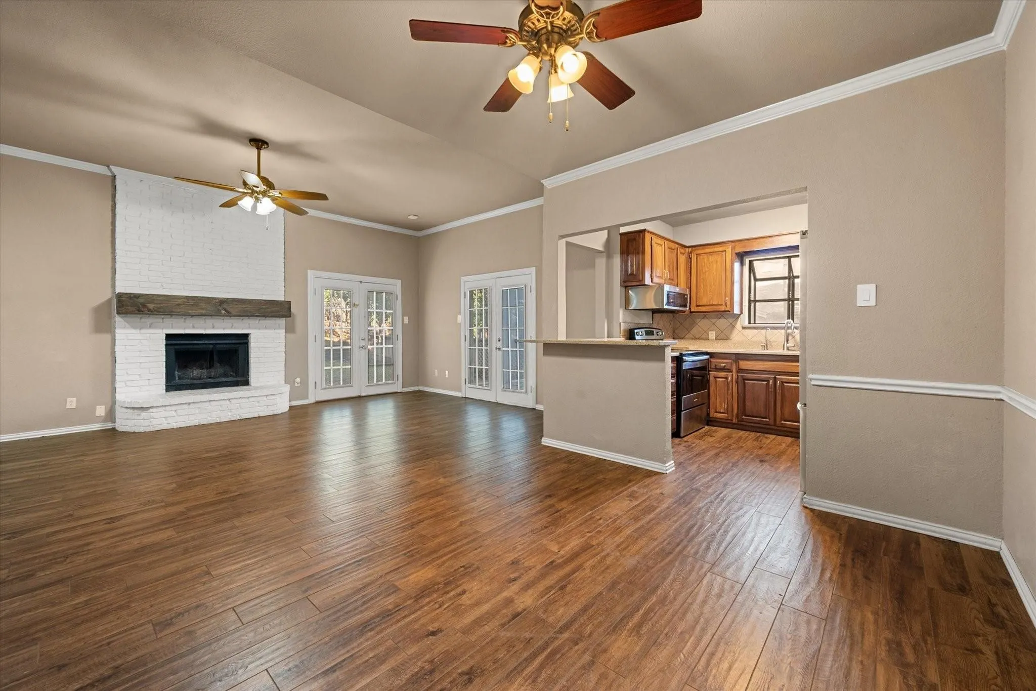 Living area featuring wood-finish flooring, a white brick fireplace with a wood mantle, and a ceiling fan