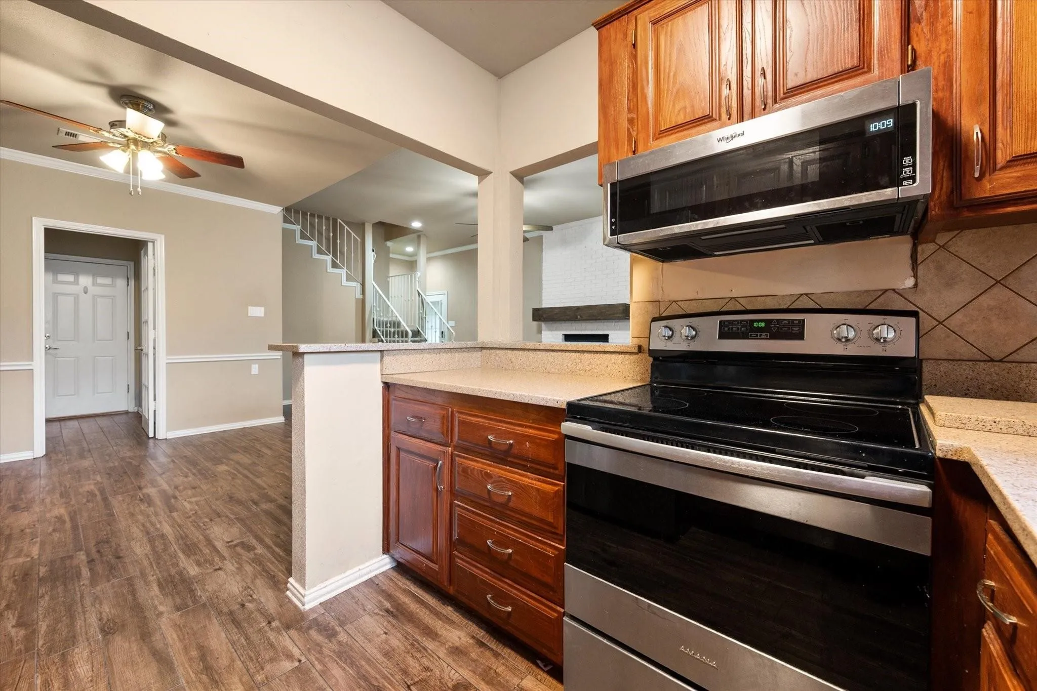 Kitchen featuring wood-finish cabinetry, light-toned countertops, a geometric tile backsplash, and stainless steel appliances including a French door refrigerator and a dishwasher